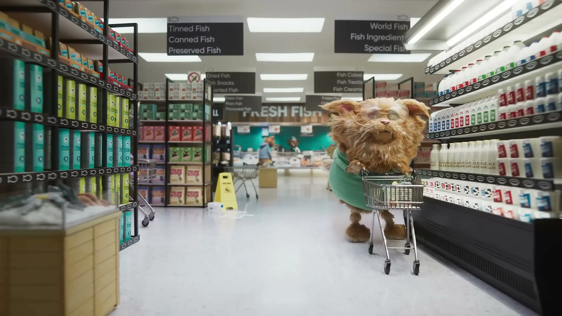 A fluffy, orange, dog-like creature wearing glasses and a green sweater pushes a small shopping cart down a grocery store aisle, looking around with a confused expression.