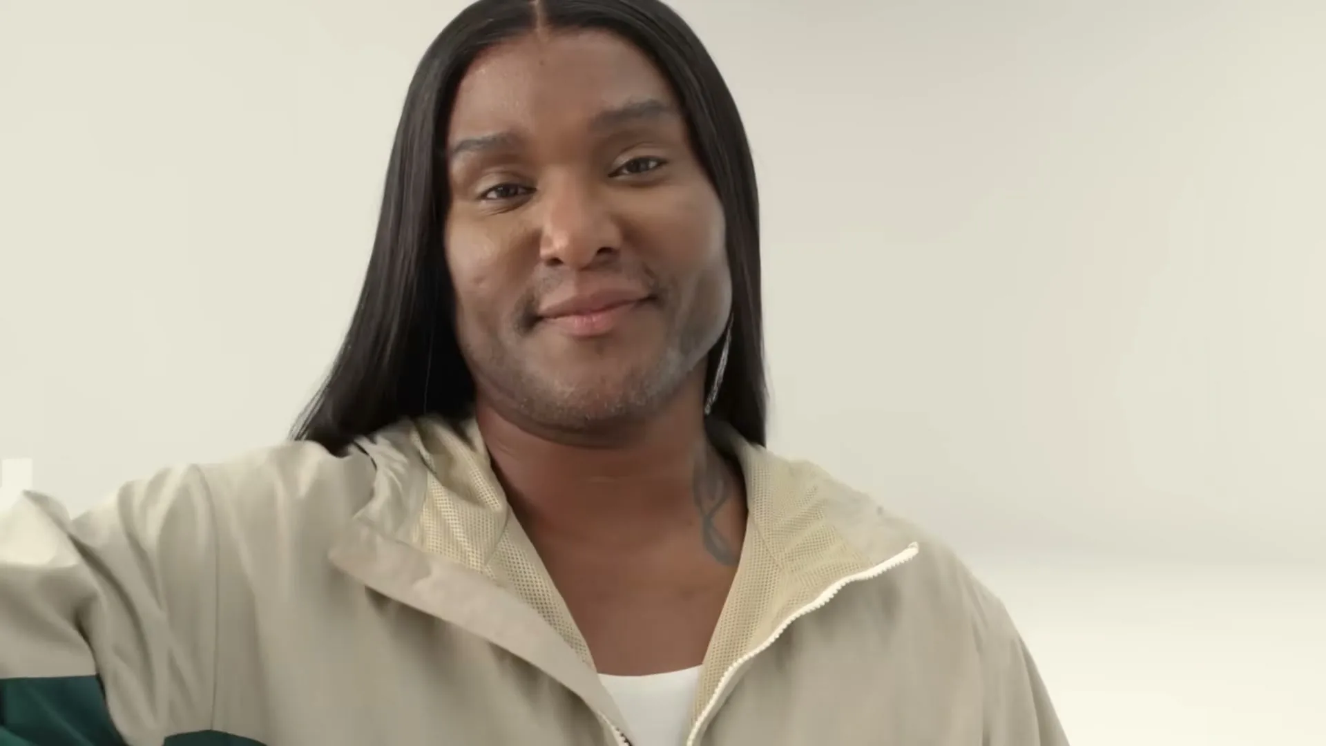 A person with long dark hair and a light jacket smiles at the camera in a bright, minimalist setting.
