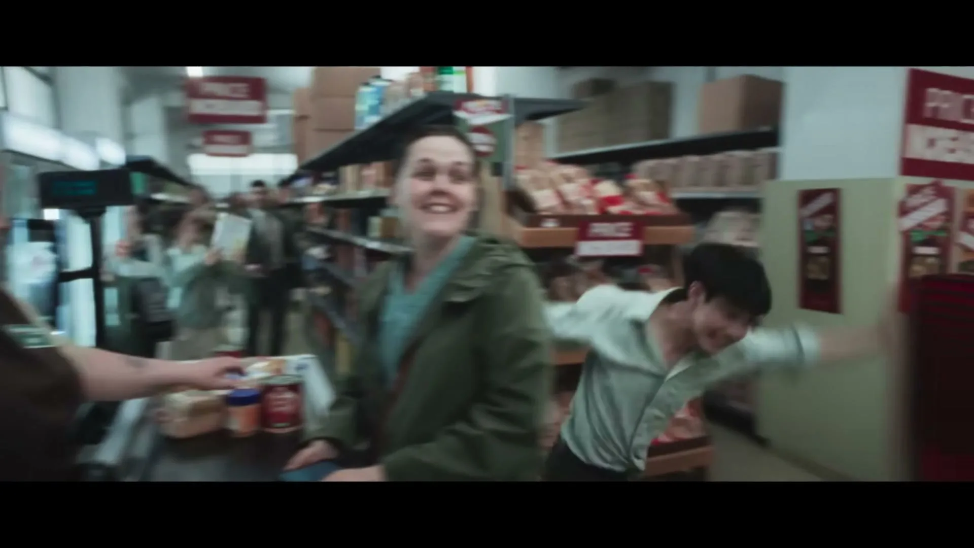 A cashier and a customer talk at a checkout counter in a grocery store, while other shoppers dance chaotically in the background, surrounded by "Price Increased" signs.