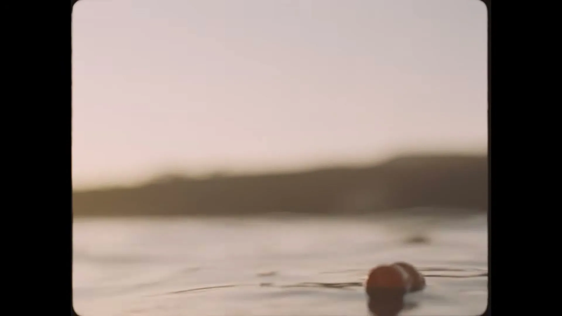 A blurry shot of a person's head and shoulders in the water, with a hazy sky and distant land in the background.
