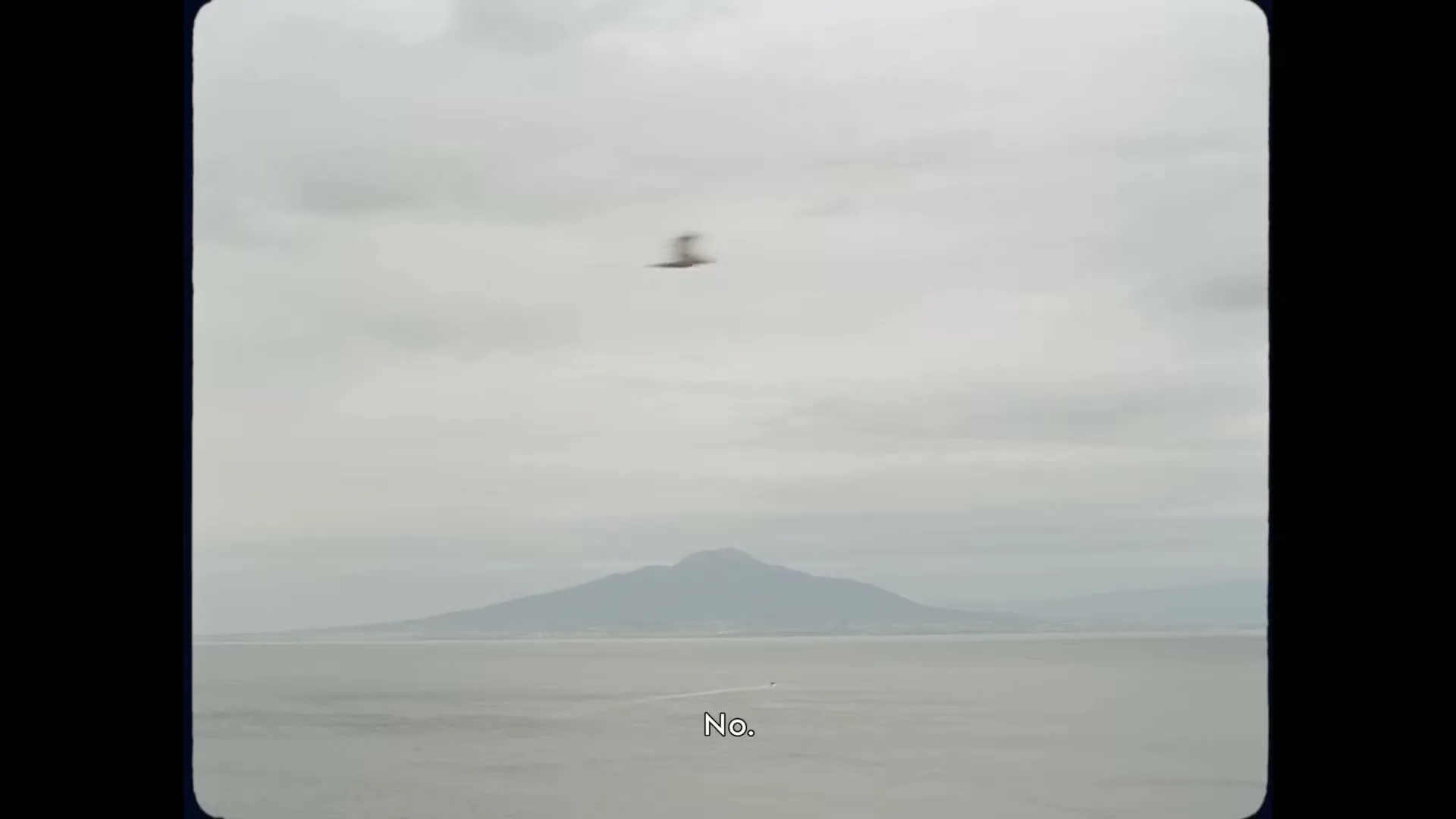 A wide shot shows a vast body of water with a distant mountain under a cloudy sky, with a small boat moving across the water.