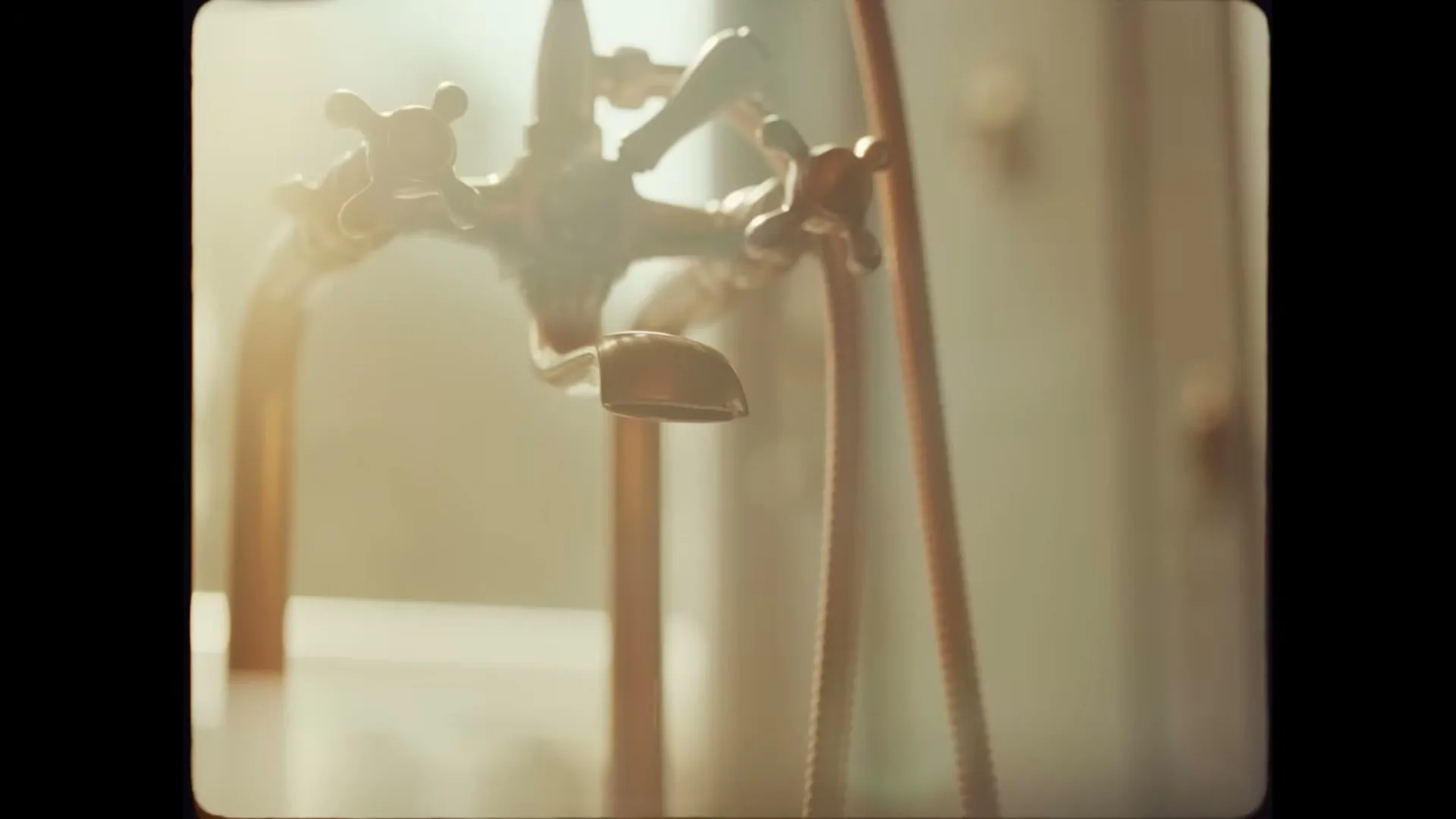 A close-up shot of a vintage-style brass faucet with a single drop of water falling, bathed in warm, natural light.