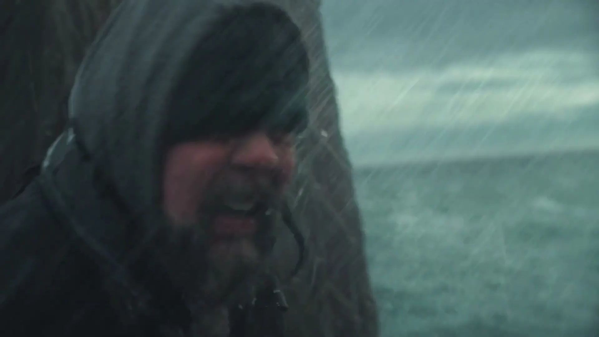 A fisherman in a hooded jacket and blue gloves is seen on a boat in heavy rain, looking distressed as he touches his head.