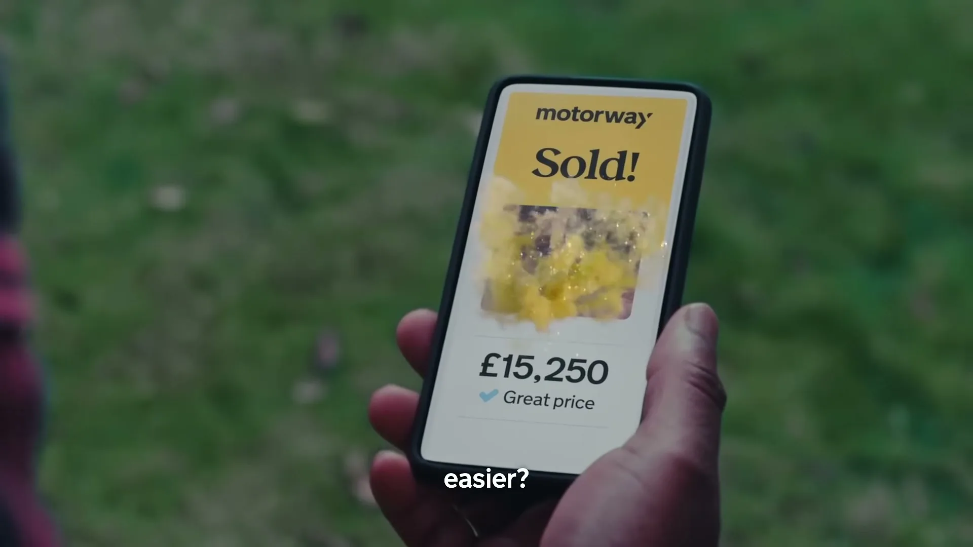 A person holds a smartphone displaying the Motorway app, showing a car sold for 
£15,250 with a "Great price" checkmark, against a blurred green background.