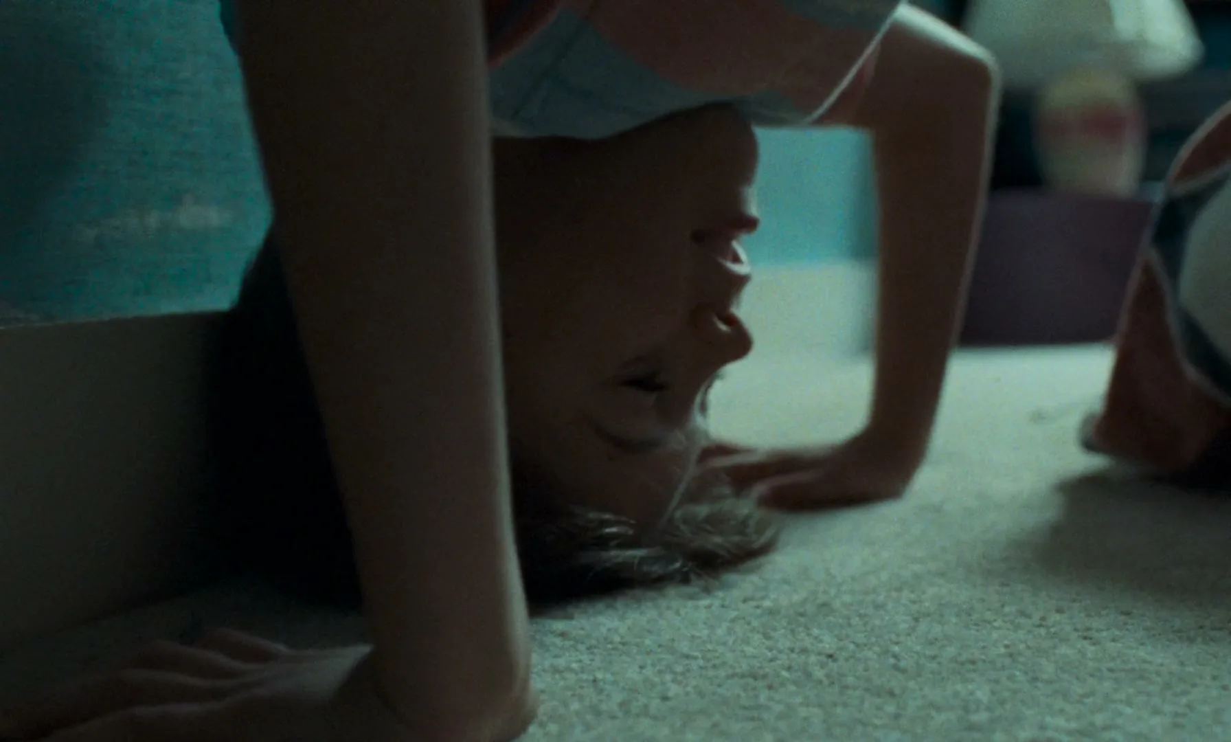 A child with light brown hair, wearing a striped t-shirt, is upside down on a carpeted floor, with their hands and head on the ground.