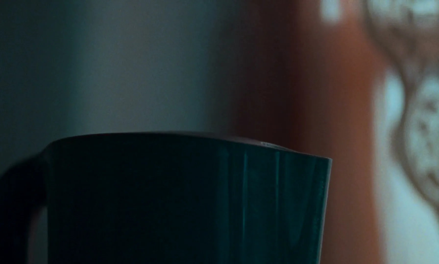 A dark green kettle is seen in a close-up shot, with a blurry, warm-toned background, suggesting an interior setting.