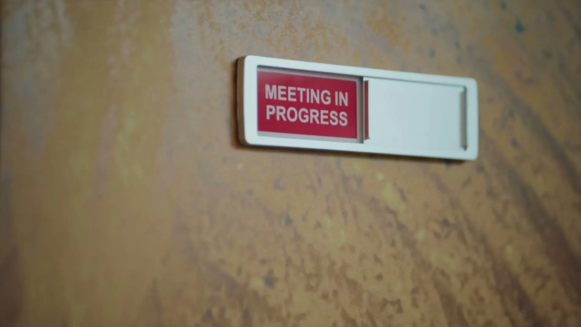 A close-up shot of a "Meeting in Progress" sign on a wooden door, indicating a busy office environment.