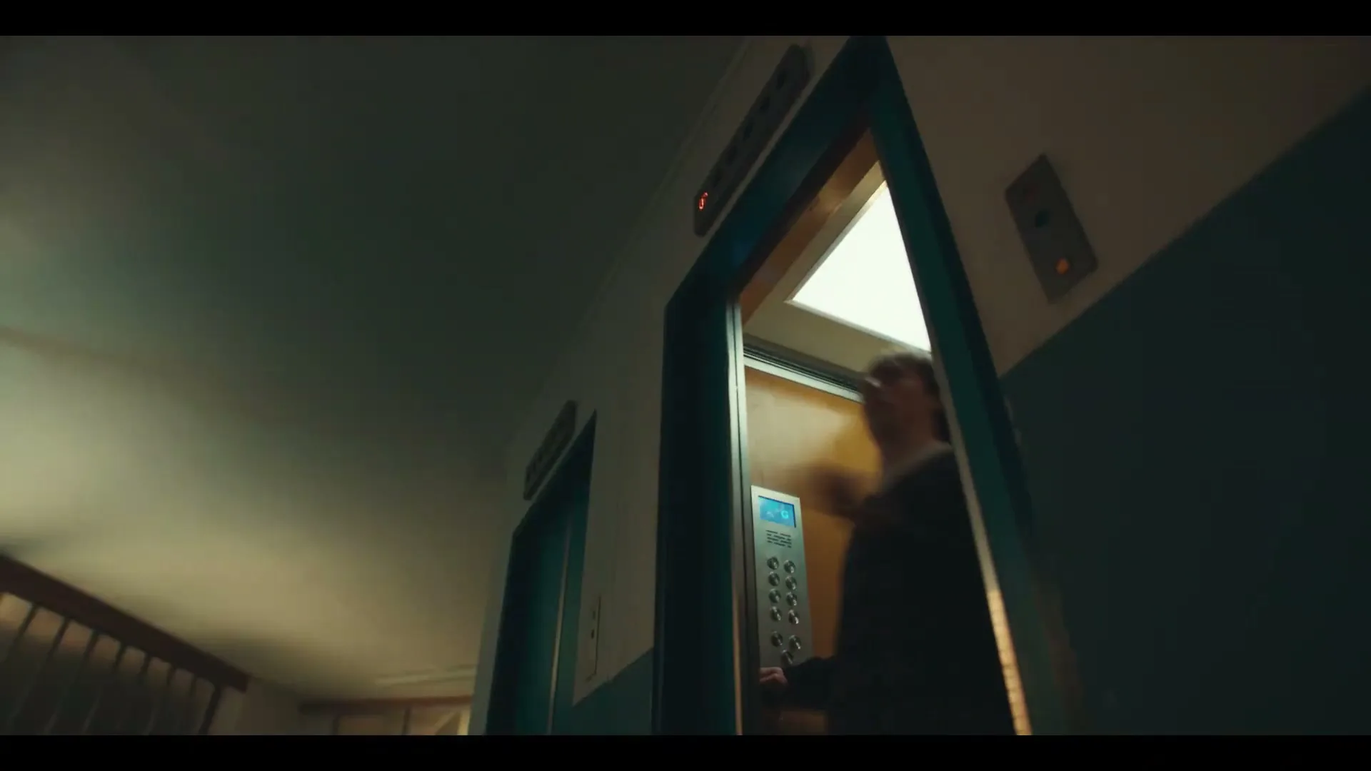 A low-angle shot shows an old elevator door opening, revealing a person inside, then quickly closing in a dimly lit hallway.