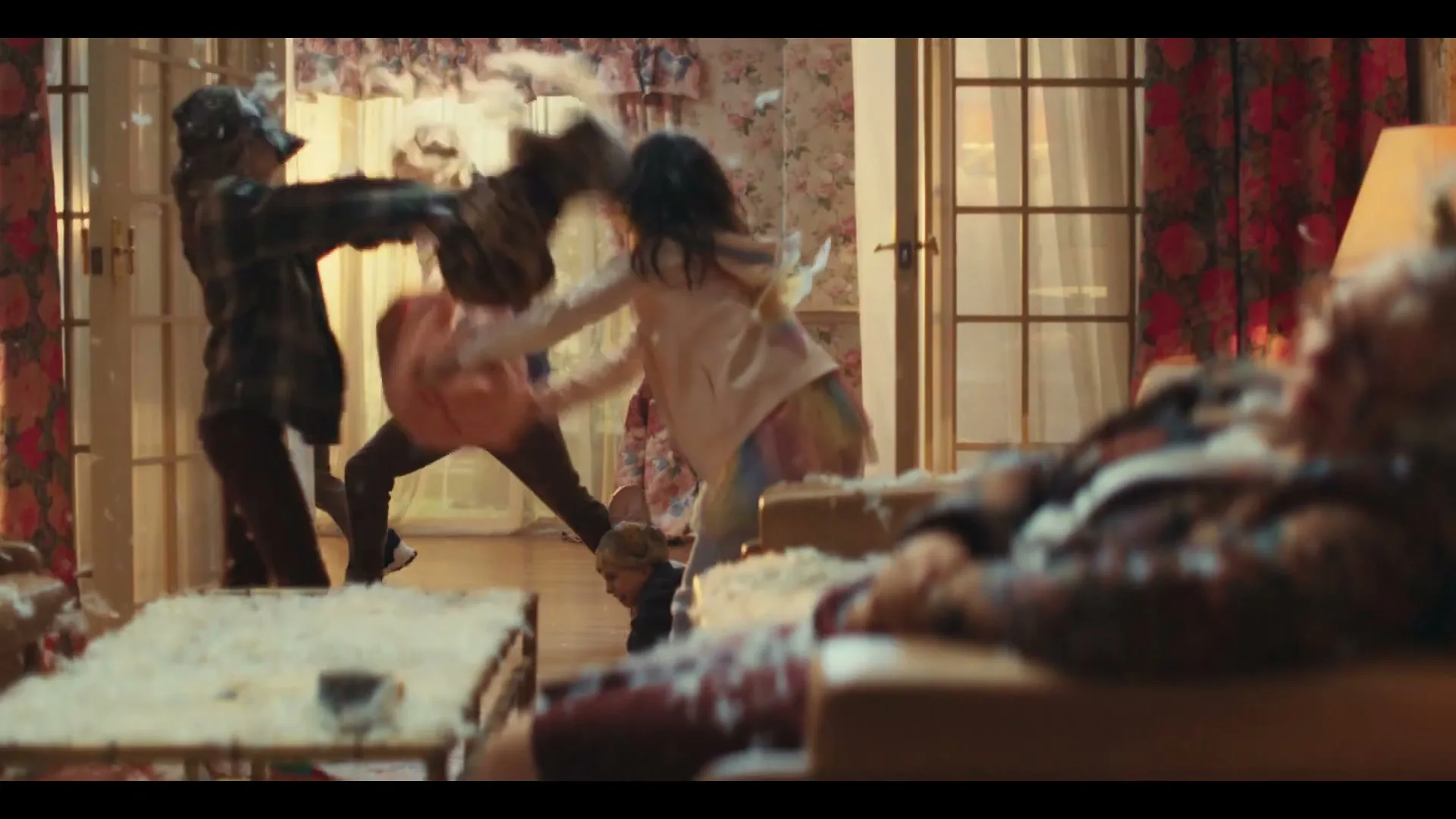 A family of four, including a father, two children, and a baby, are having a chaotic pillow fight in their living room, with feathers flying everywhere.
