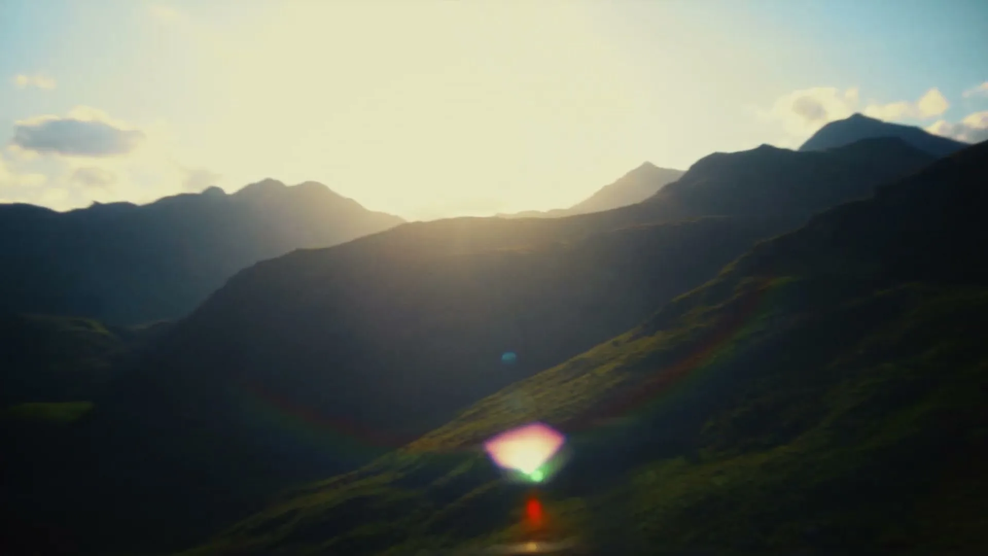 The sun sets behind a range of mountains, casting long shadows and creating a lens flare in the foreground.