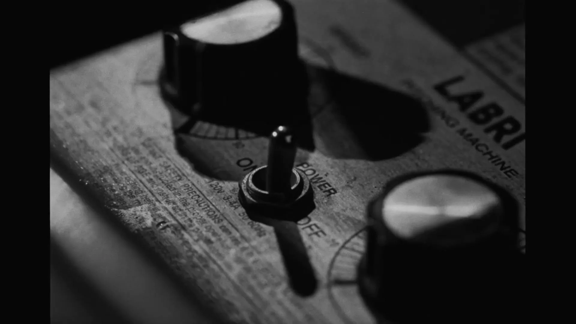 A close-up shot of a vintage machine's control panel, featuring a toggle switch and rotary knobs, in black and white.