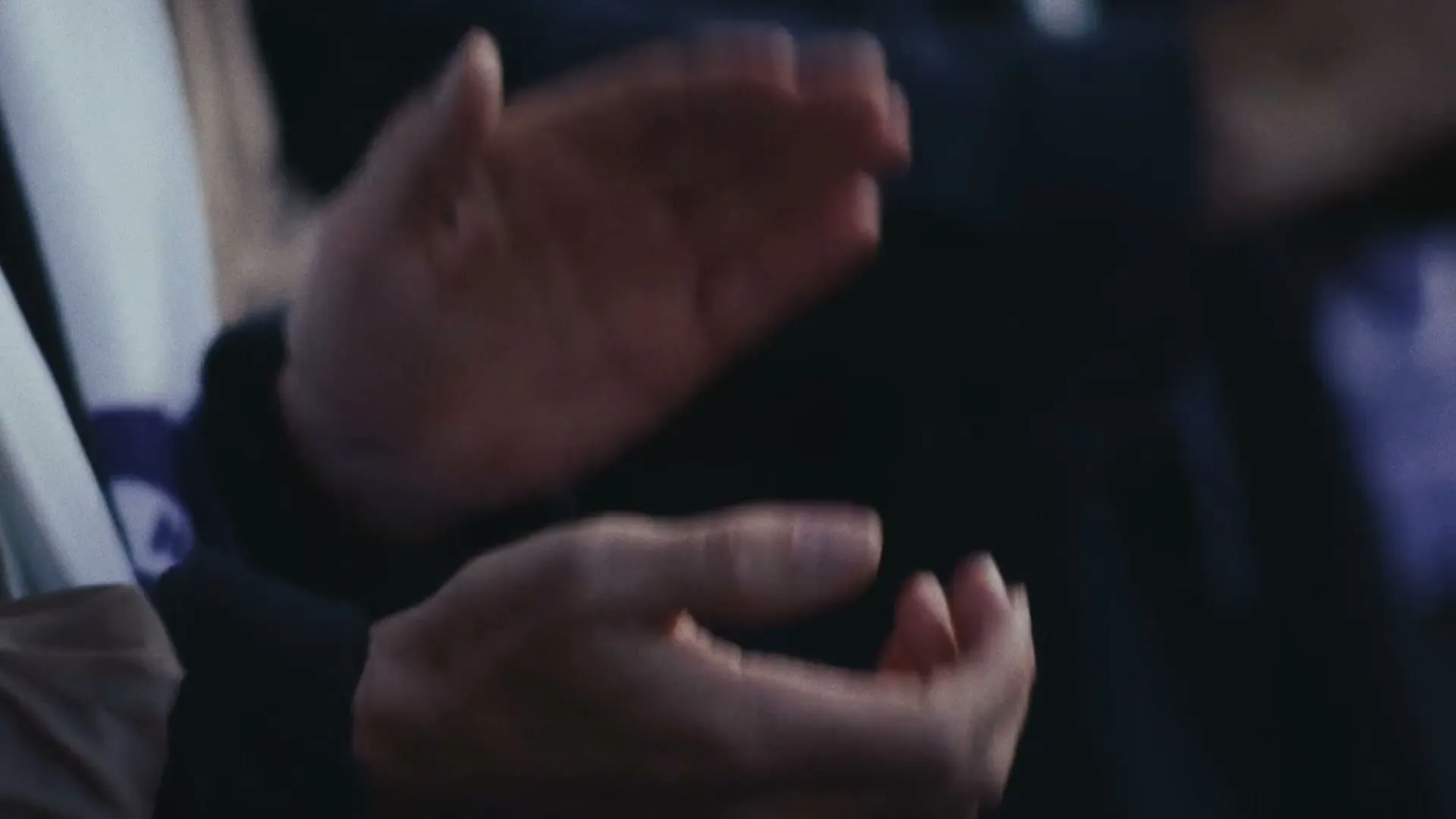 A person's hands are seen clapping in a medium closeup shot, likely at a sporting event or public gathering.