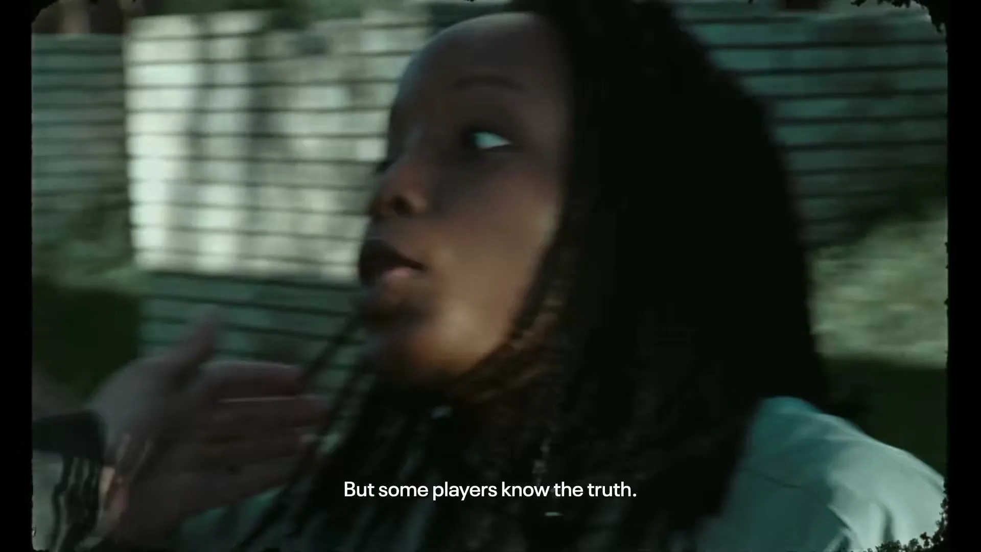 A young Black woman with dreadlocks looks up and to the right, speaking with an intense expression, outdoors during the day.