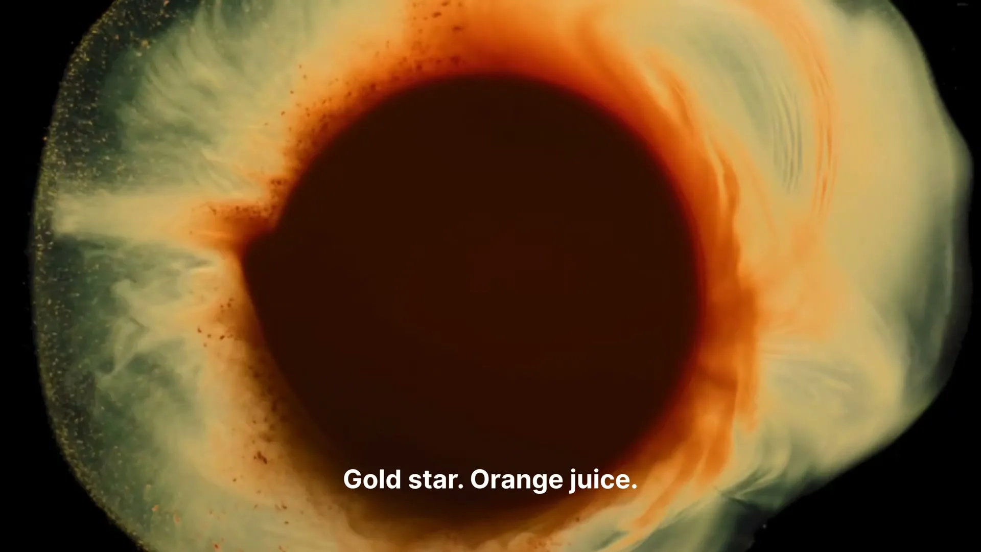 A macro shot shows orange and white paint swirling and mixing around a dark central void, resembling an eye or a celestial body.