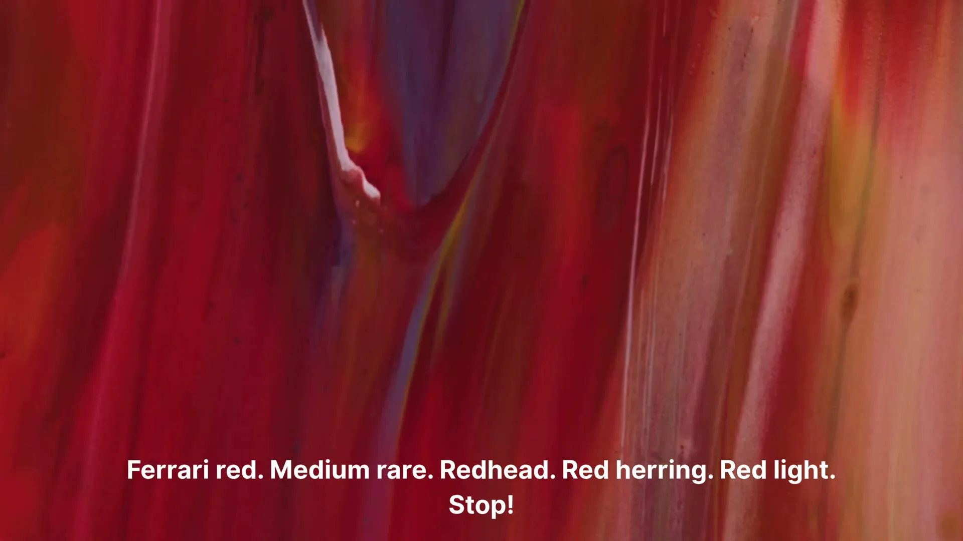 A close-up shot of abstract red paint flowing and mixing with other colors, with white text overlaid on the bottom of the screen.