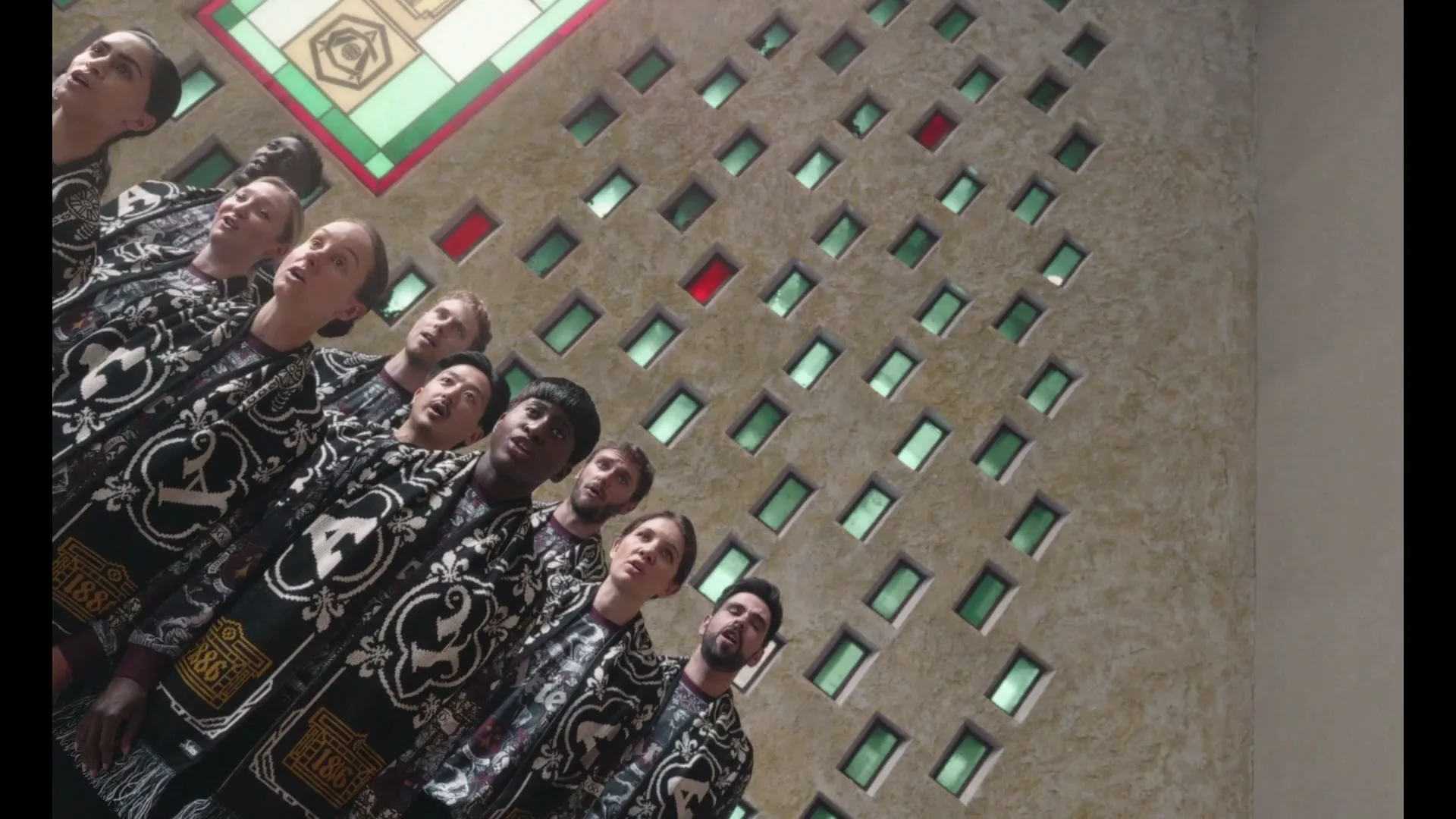 A diverse group of people, dressed in ornate black and white robes, stand in a choir formation, looking upwards in a grand, architecturally unique building.