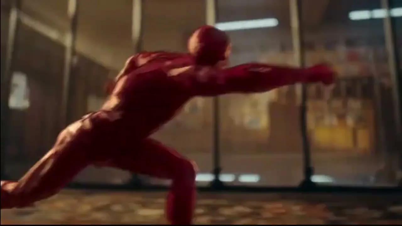 A red, muscular, CGI superhero-like figure falls and then quickly gets up and runs across a patterned floor in a large, open room with tall windows.