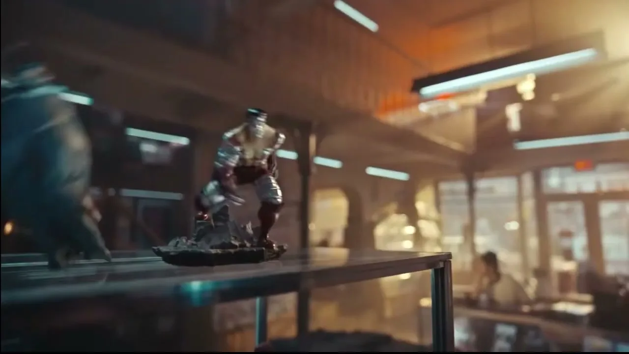 A detailed action figure of a superhero in red and silver armor stands on a display shelf in a sunlit store, then falls off.
