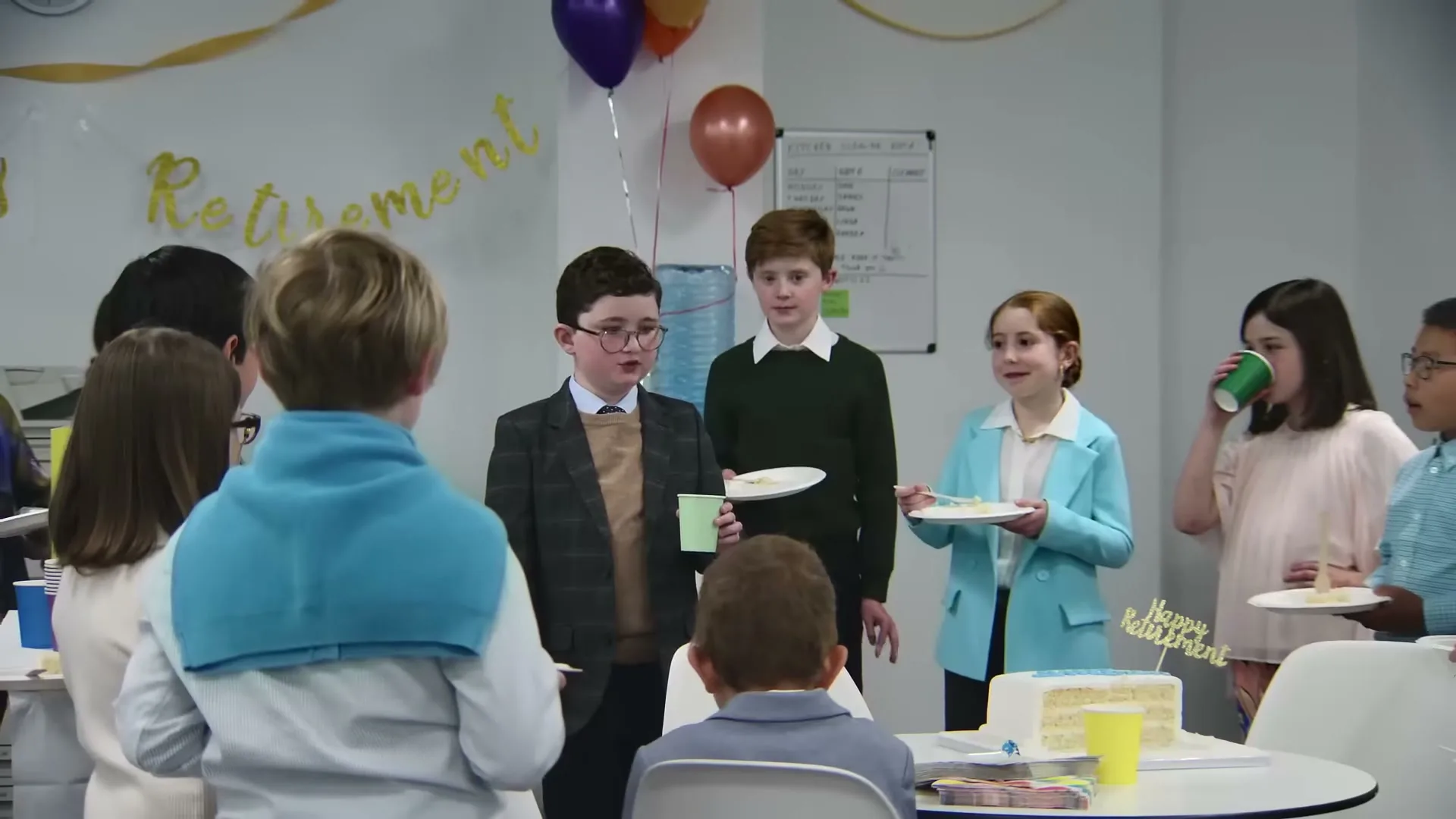 A group of children dressed in business attire are gathered around a table, celebrating a "Retirement" party in an office setting.