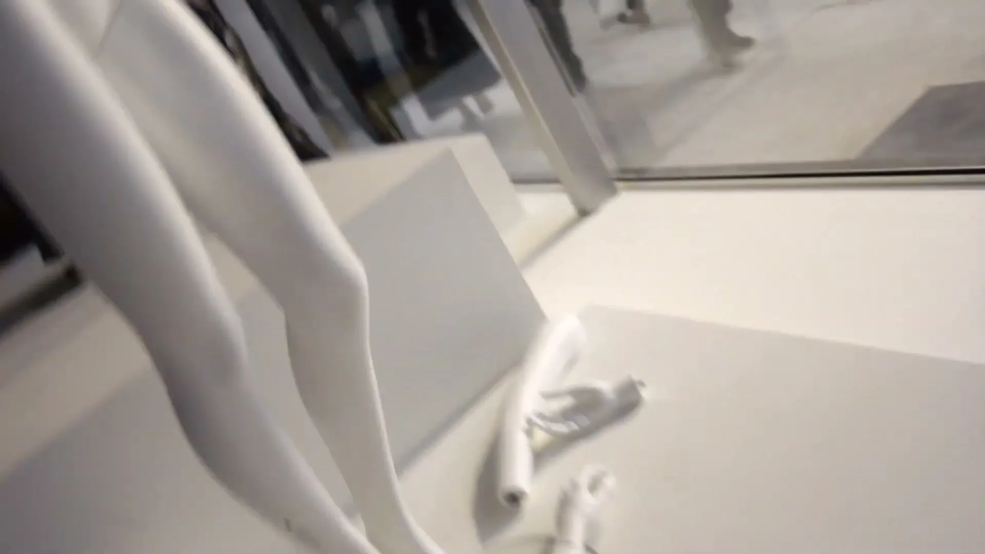 A blurry shot of white mannequin legs and arms in a store window, with reflections of people walking by outside.