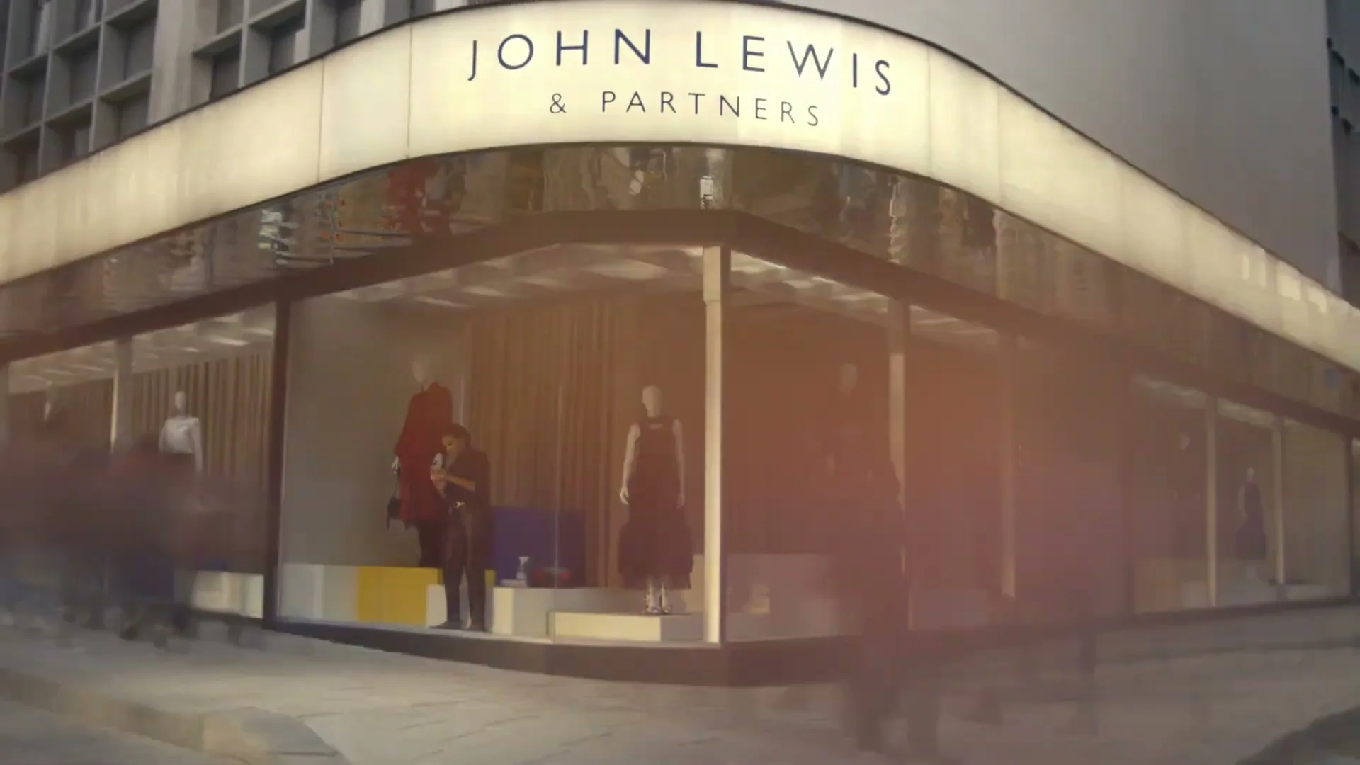 A time-lapse shot of a John Lewis department store window display changing from day to night, with blurred people passing by.