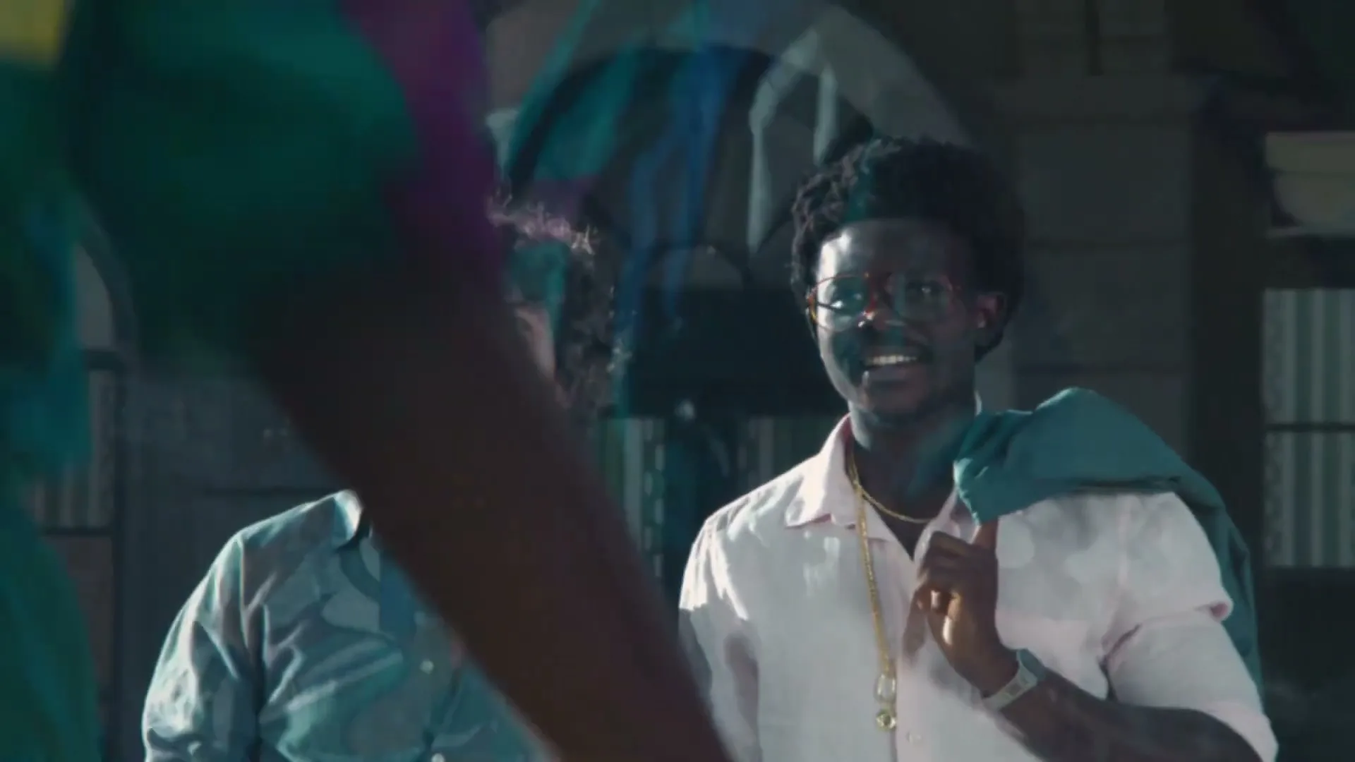 Two men, one with curly hair and a patterned shirt, the other with an afro and glasses, laugh and smile while looking at someone off-screen in an interior setting.