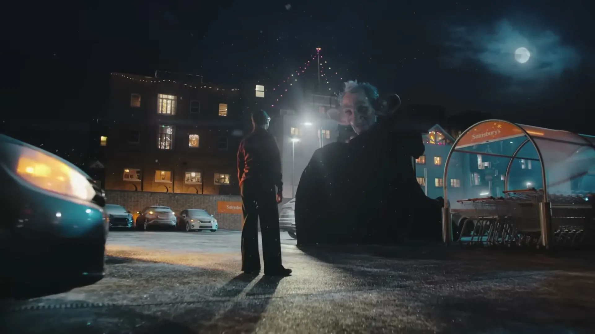A young boy stands in a parking lot at night, looking up at a giant, elderly man who is slowly appearing from the shadows.