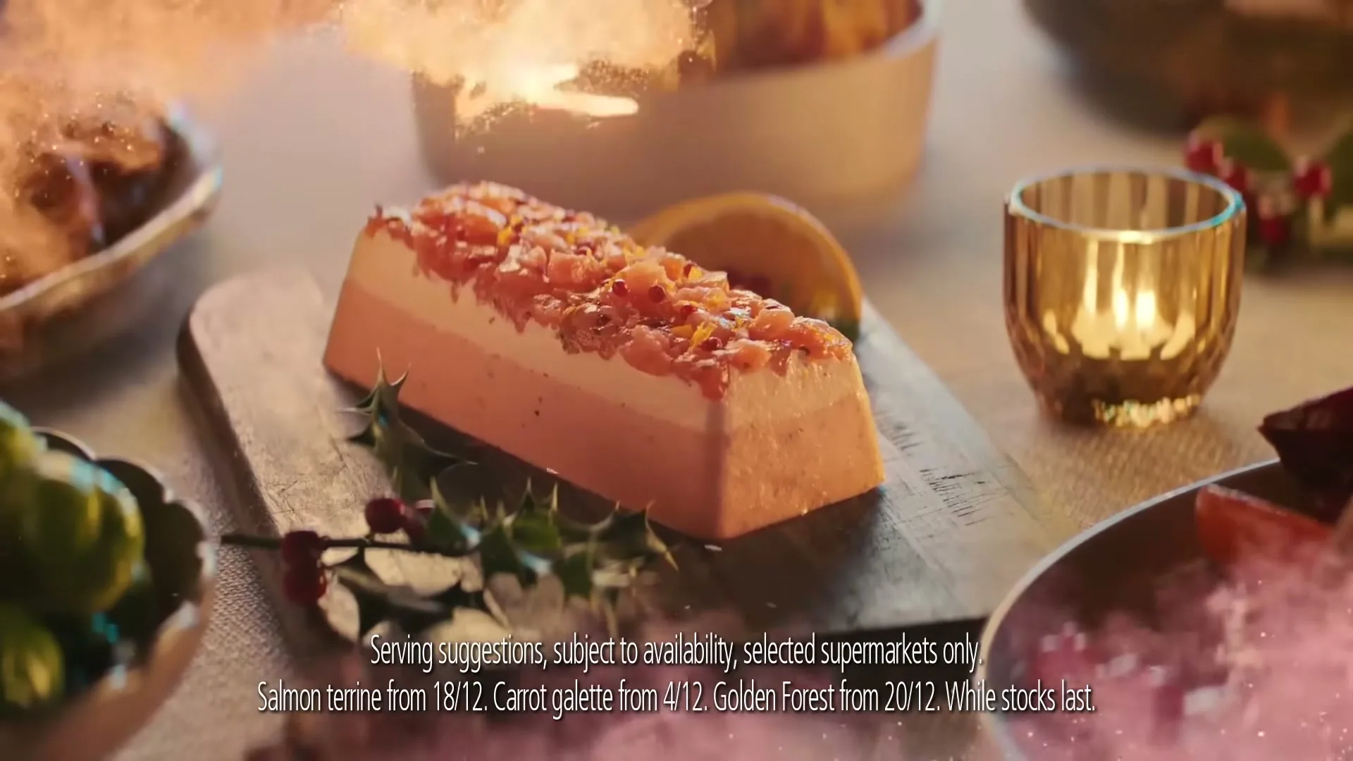 A salmon terrine with holly garnish is presented on a wooden board on a festive table, with golden light and glitter falling around it.