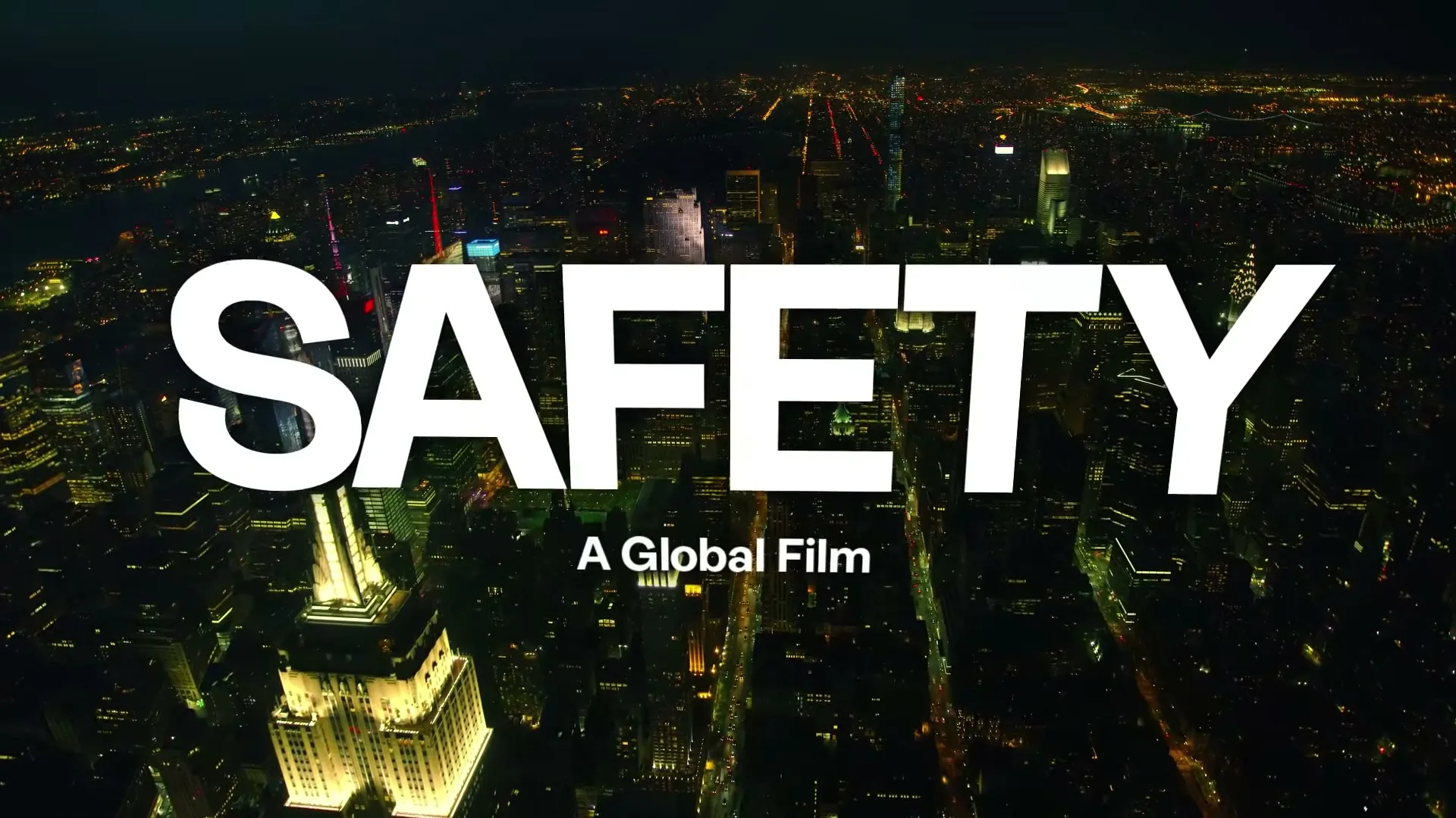 An aerial view of a city at night with bright lights, featuring the words "SAFETY A Global Film" overlaid in white text.