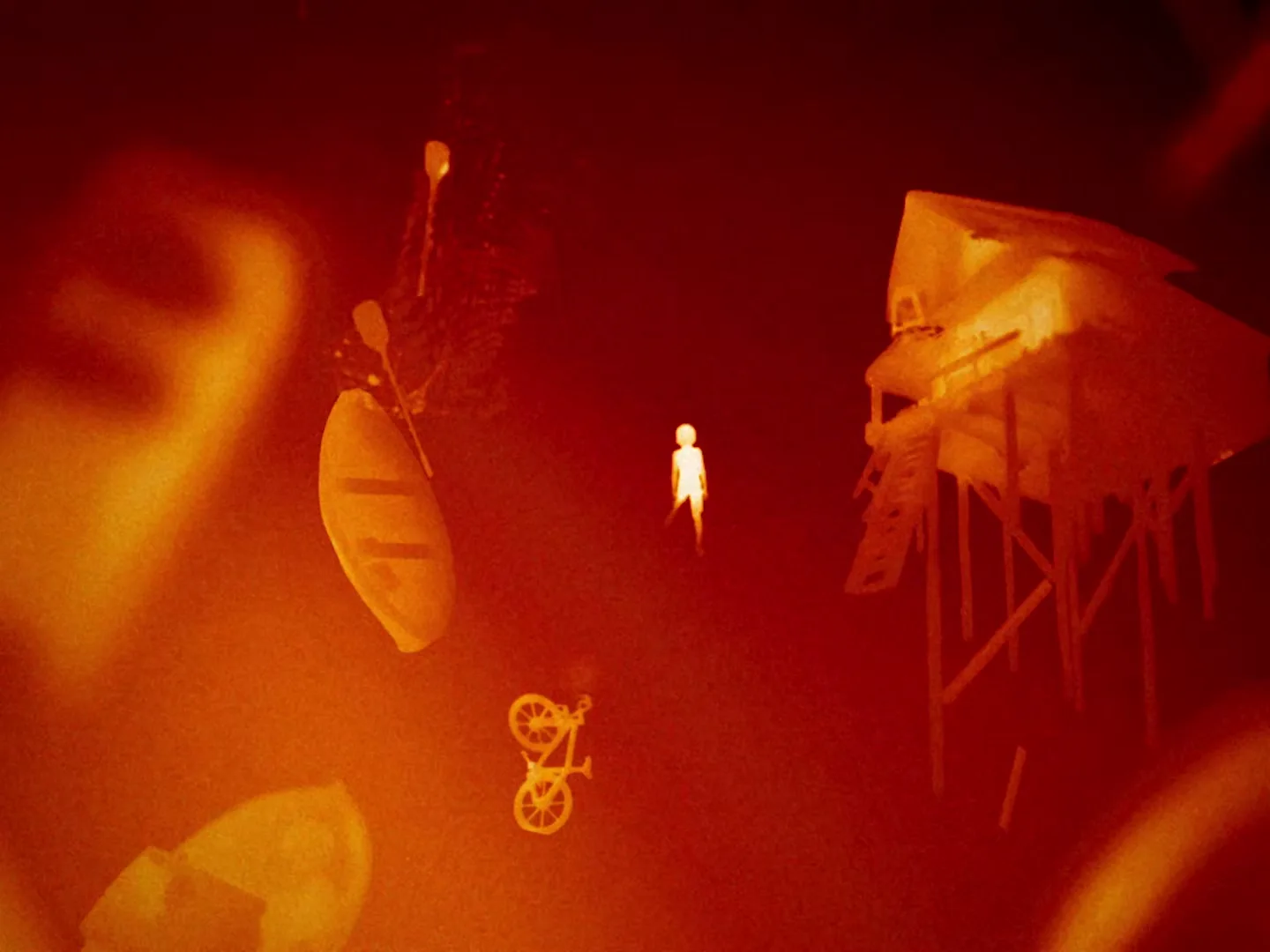 A small, glowing human figure floats in a dark red, smoky void, surrounded by miniature, glowing objects like a house, a boat, and a bicycle.