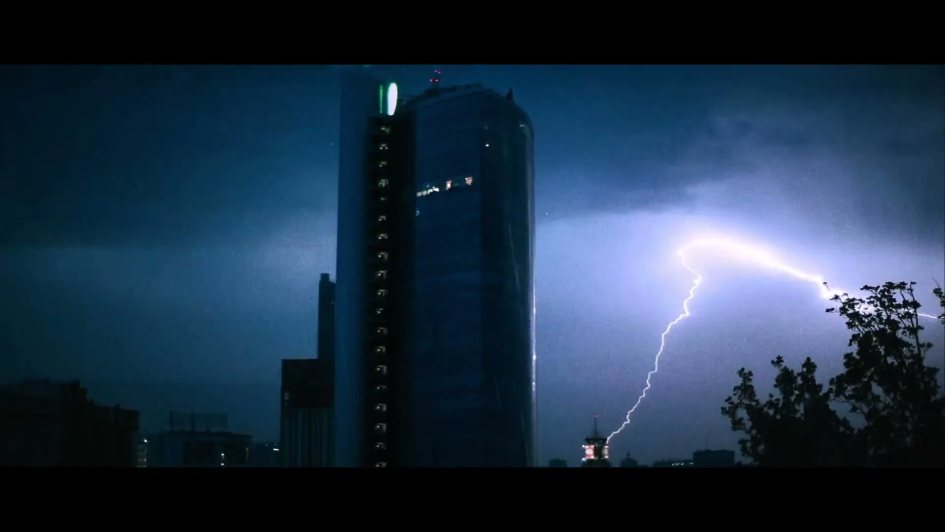 A tall, dark skyscraper stands against a stormy blue sky as a bright lightning bolt flashes across the right side of the frame.