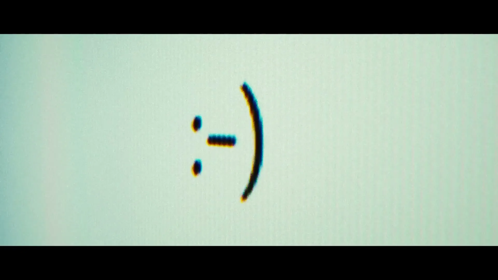 A close-up shot shows a computer screen with a blinking cursor typing out a smiley face emoticon, then changing it to a neutral face.