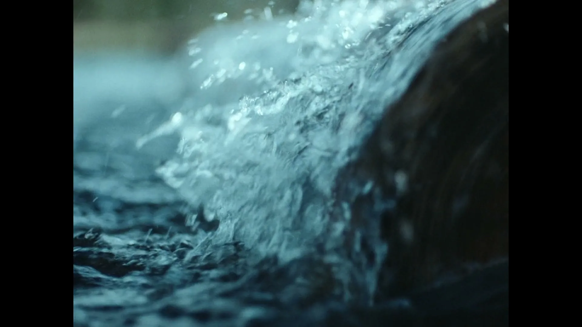 A close-up shot shows water splashing and rippling around a dark, cylindrical object, creating a dynamic and refreshing visual.