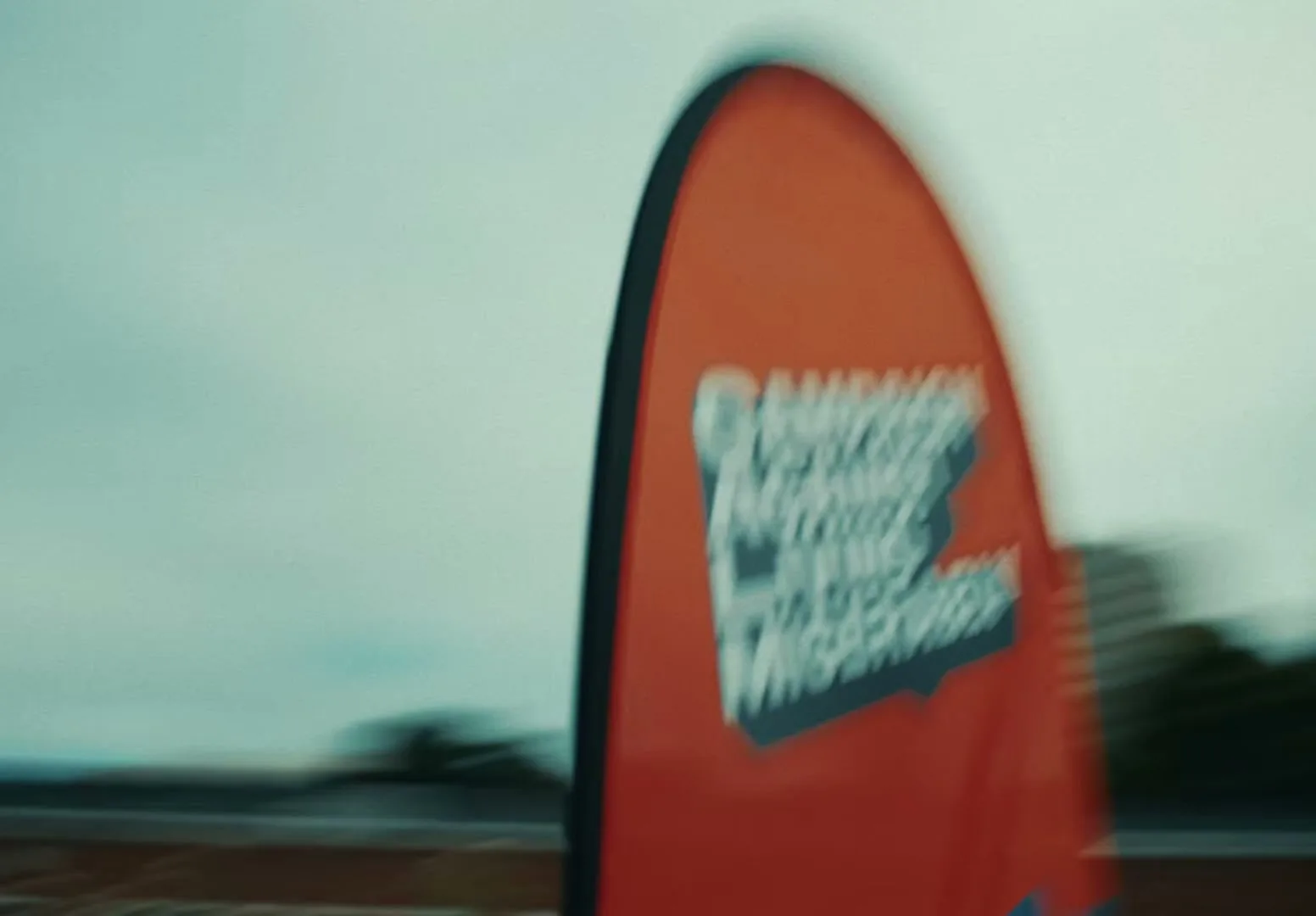 A blurry shot of an orange banner with the words "CAMPAIGN AGAINST LIVING MISERABLY" in white and blue, against a cloudy sky.