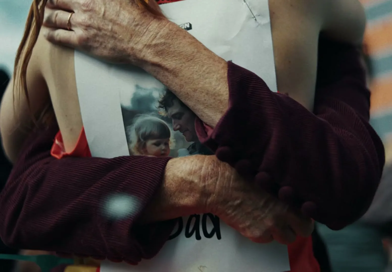 A close-up shot shows two people embracing, with one person holding a photo of a man and a child, possibly at a memorial or protest.