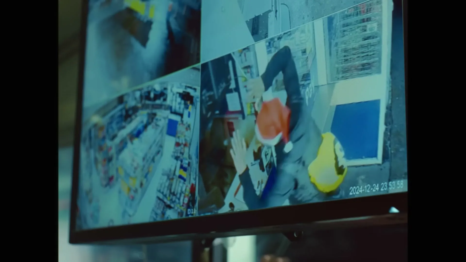 A security monitor displays multiple camera feeds, showing a person in a Santa hat and yellow vest struggling with another person in a store.