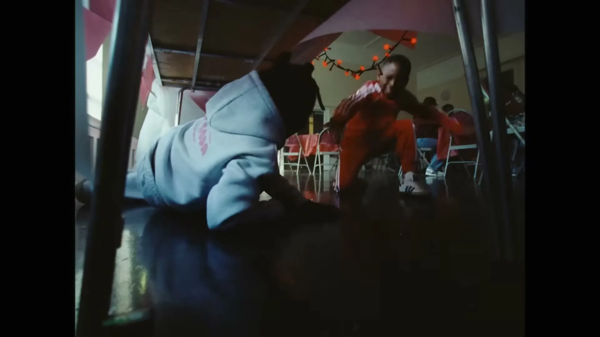 A baby in a light blue hoodie crawls on a dark floor, while a child in a red tracksuit with antlers runs in the background, in a decorated hall.