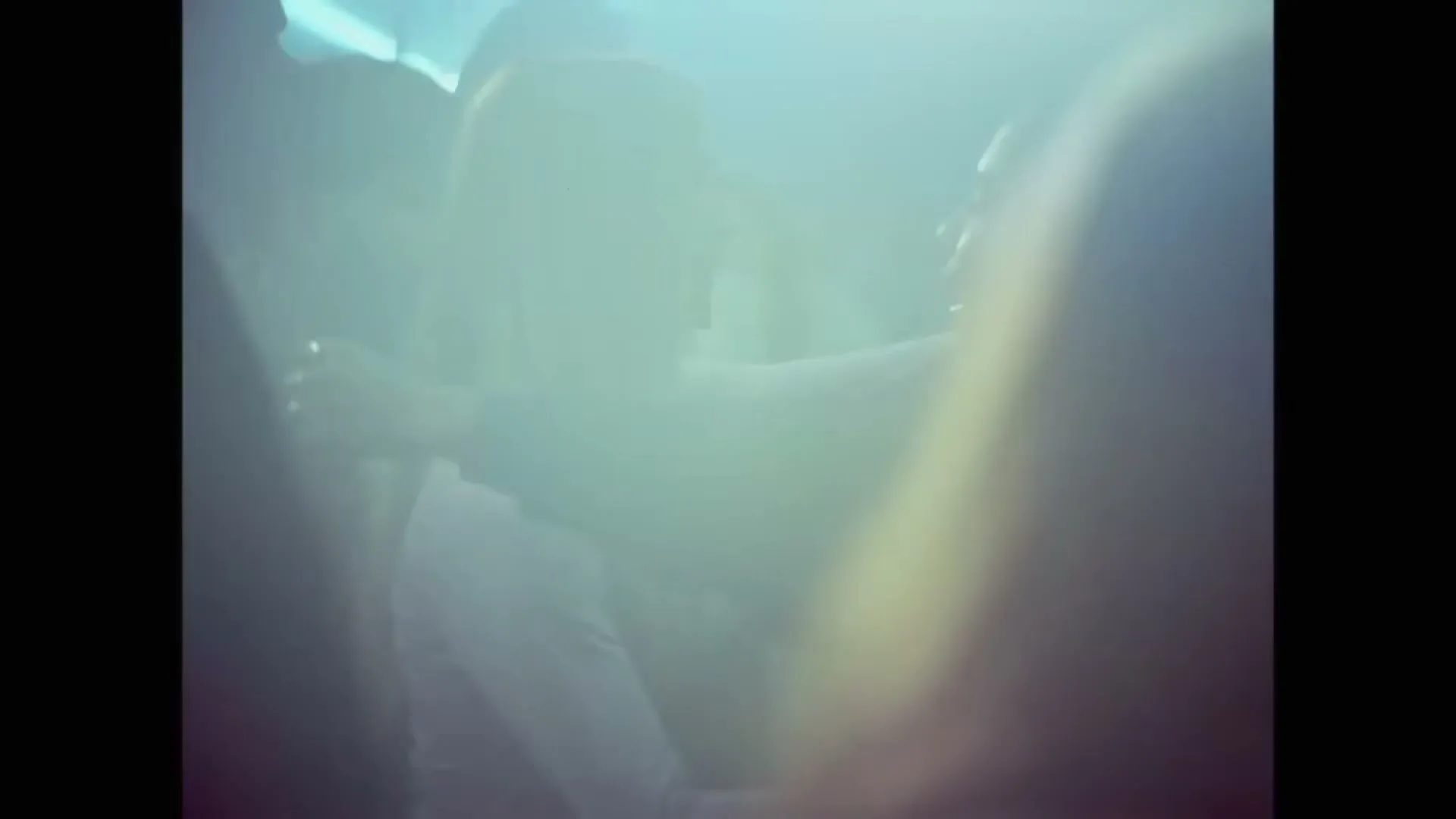 Two young women dance closely, embracing each other in a smoky, dimly lit nightclub, surrounded by other blurred figures.