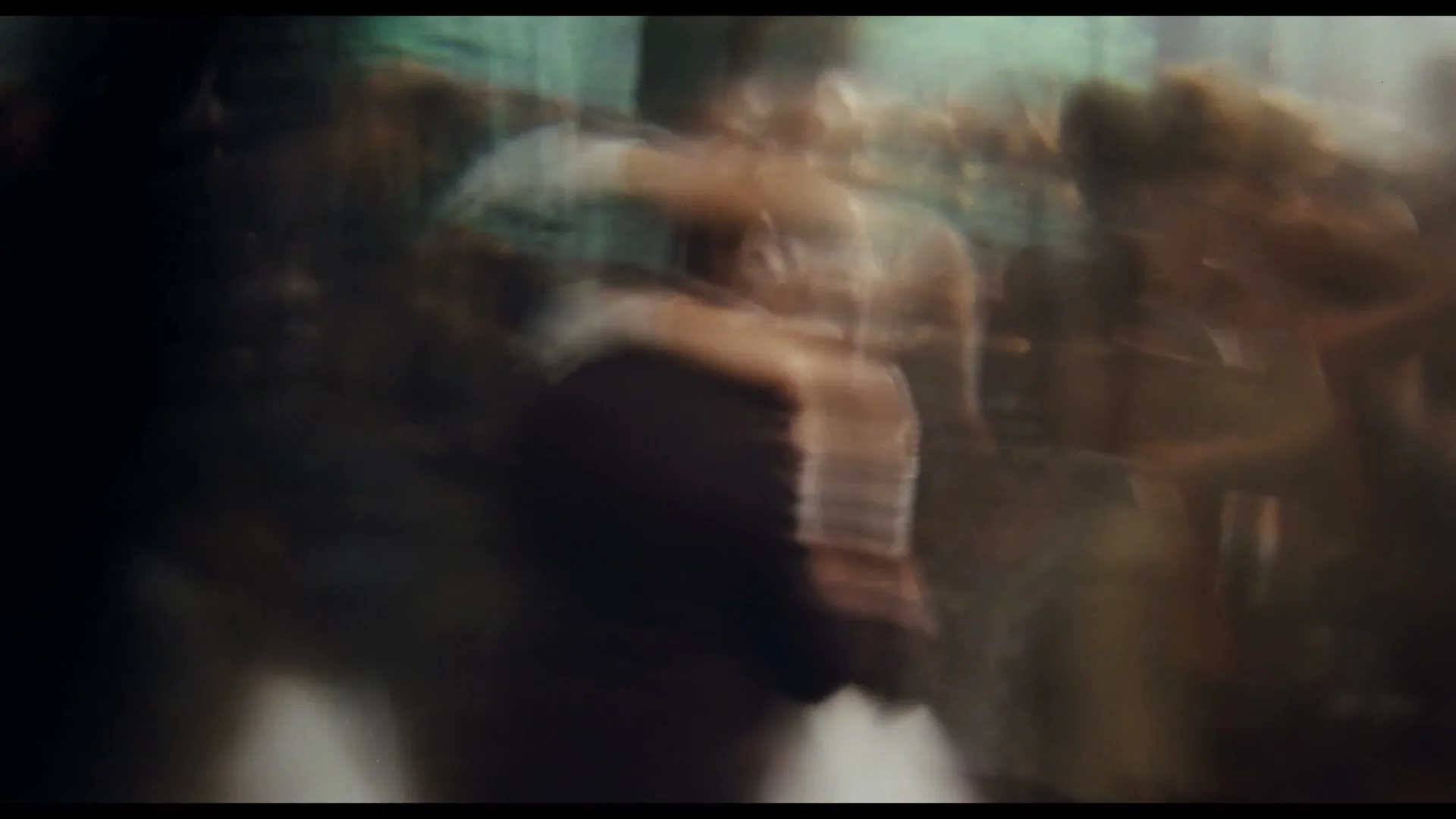 A blurry shot of a couple dancing closely, surrounded by other indistinct figures, creating a sense of movement and intimacy in a dimly lit space.