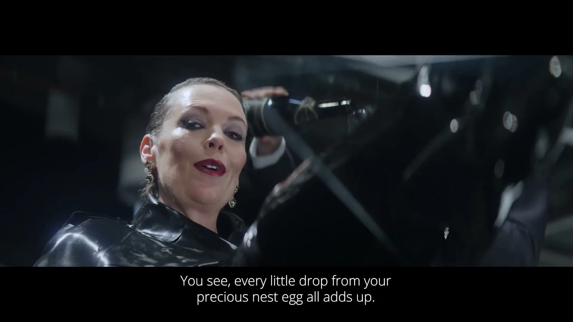 A woman in a black latex outfit smiles wickedly while holding a bottle of champagne, with a dark, industrial background.