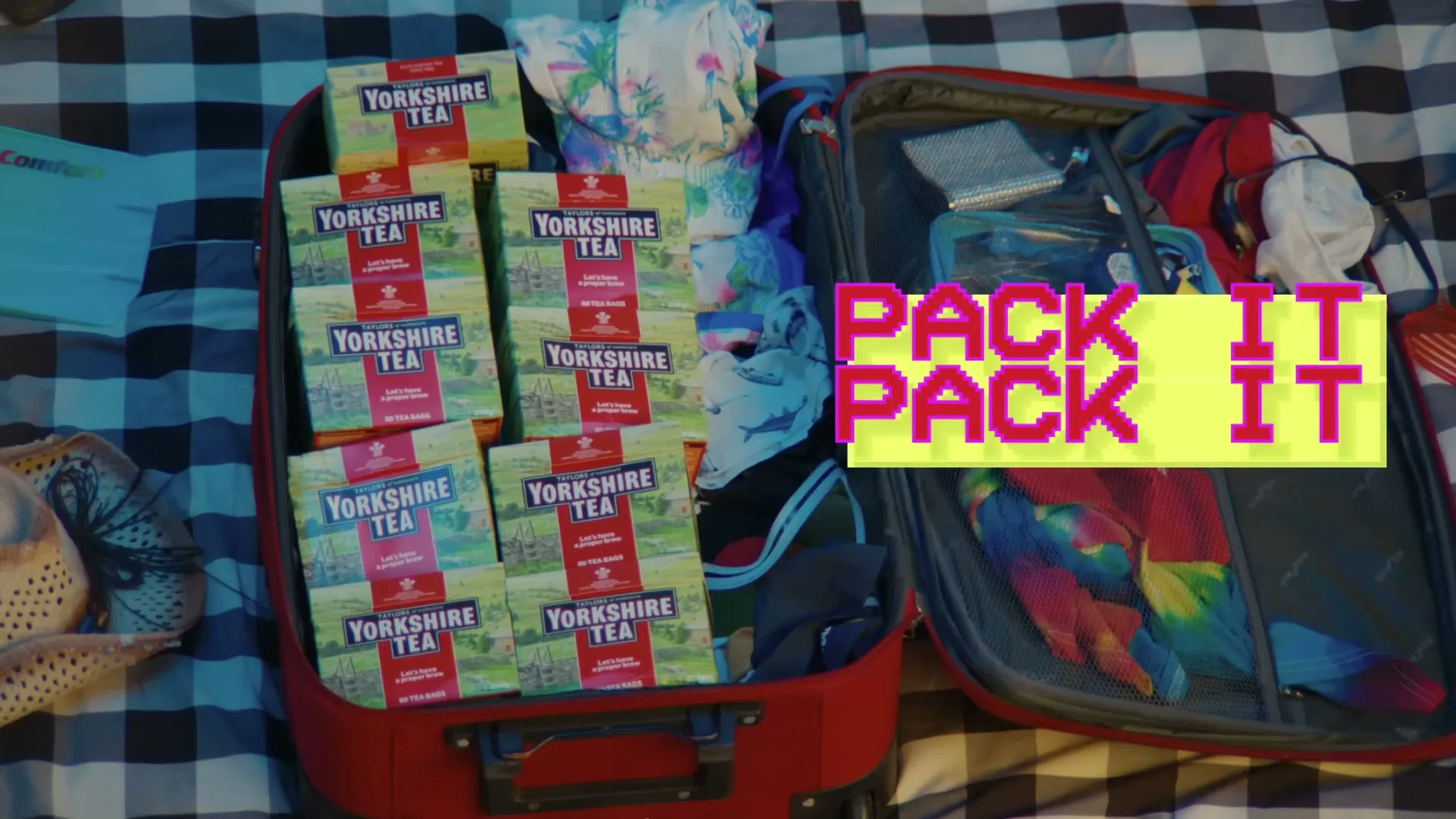 An open red suitcase is filled with many boxes of Yorkshire Tea and some clothes, with pixelated text appearing on screen.