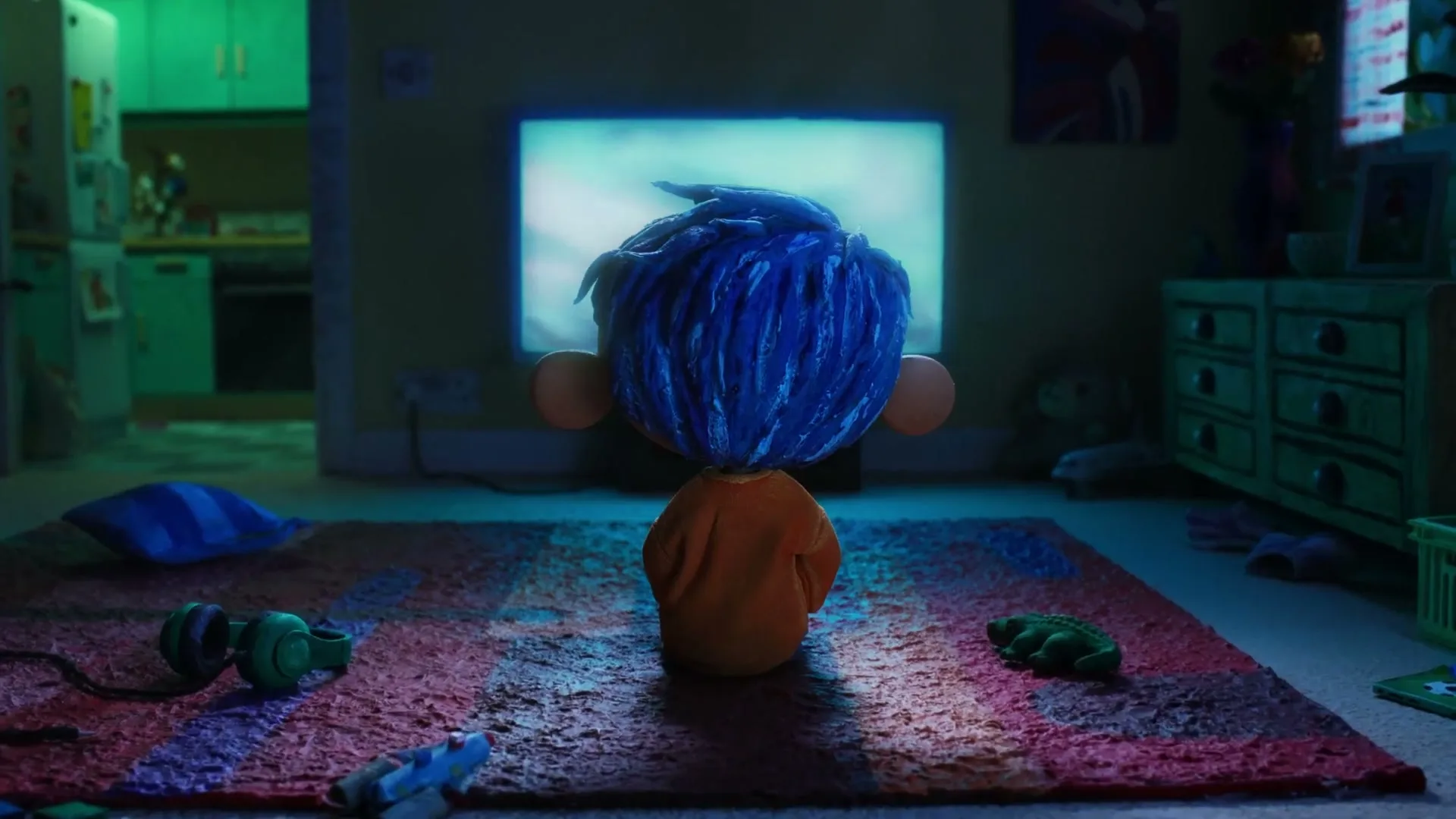 A claymation boy with blue hair sits on a rug, watching a glowing television screen in a dimly lit living room at night.