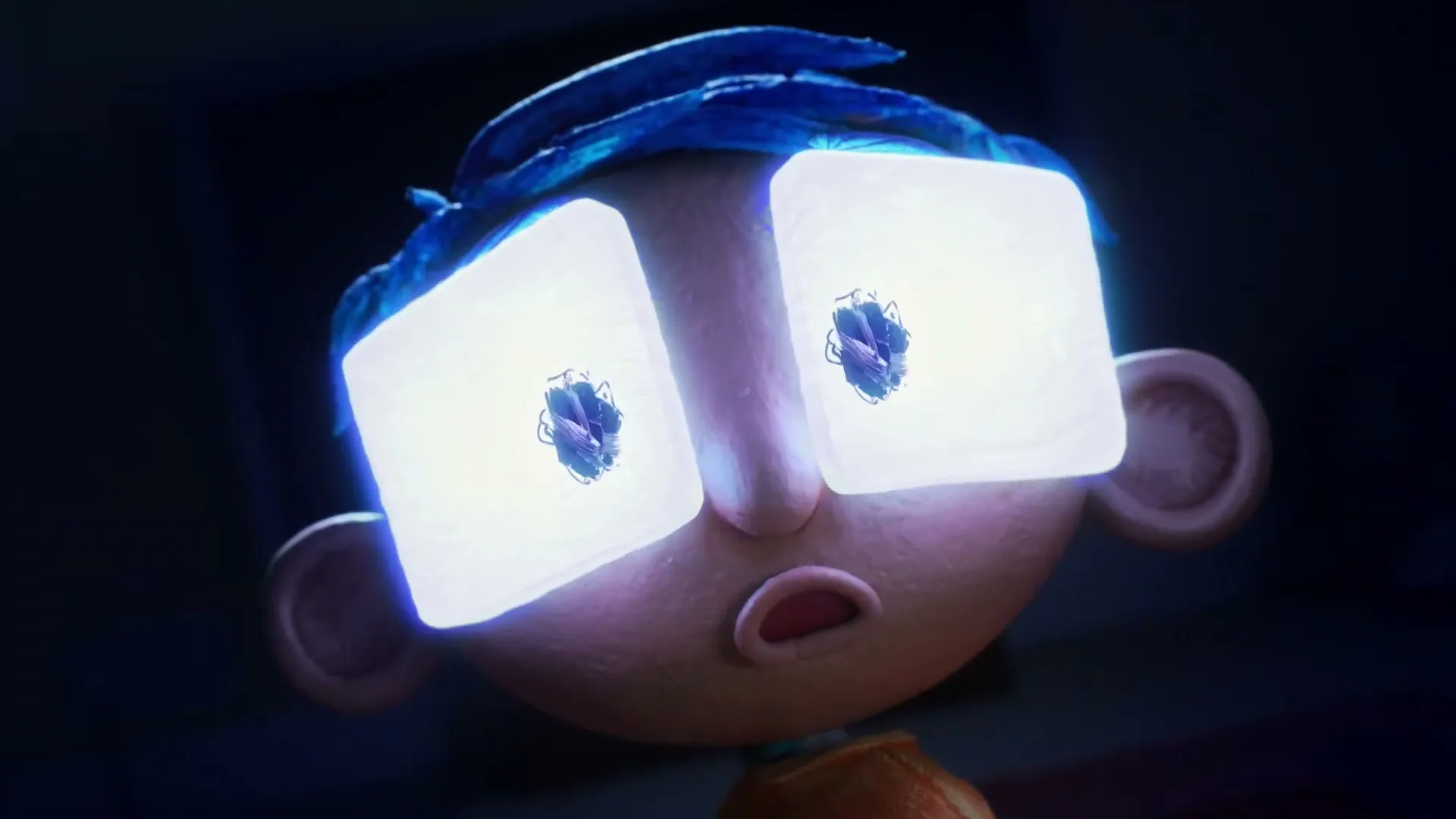 A stop-motion animated boy with blue hair and glowing square eyes looks up in a dark room, as if watching TV.