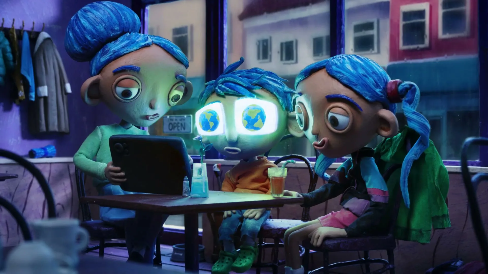 Three claymation characters with blue hair sit at a table in a cafe, looking at a tablet, as the boy's eyes glow with images of Earth.