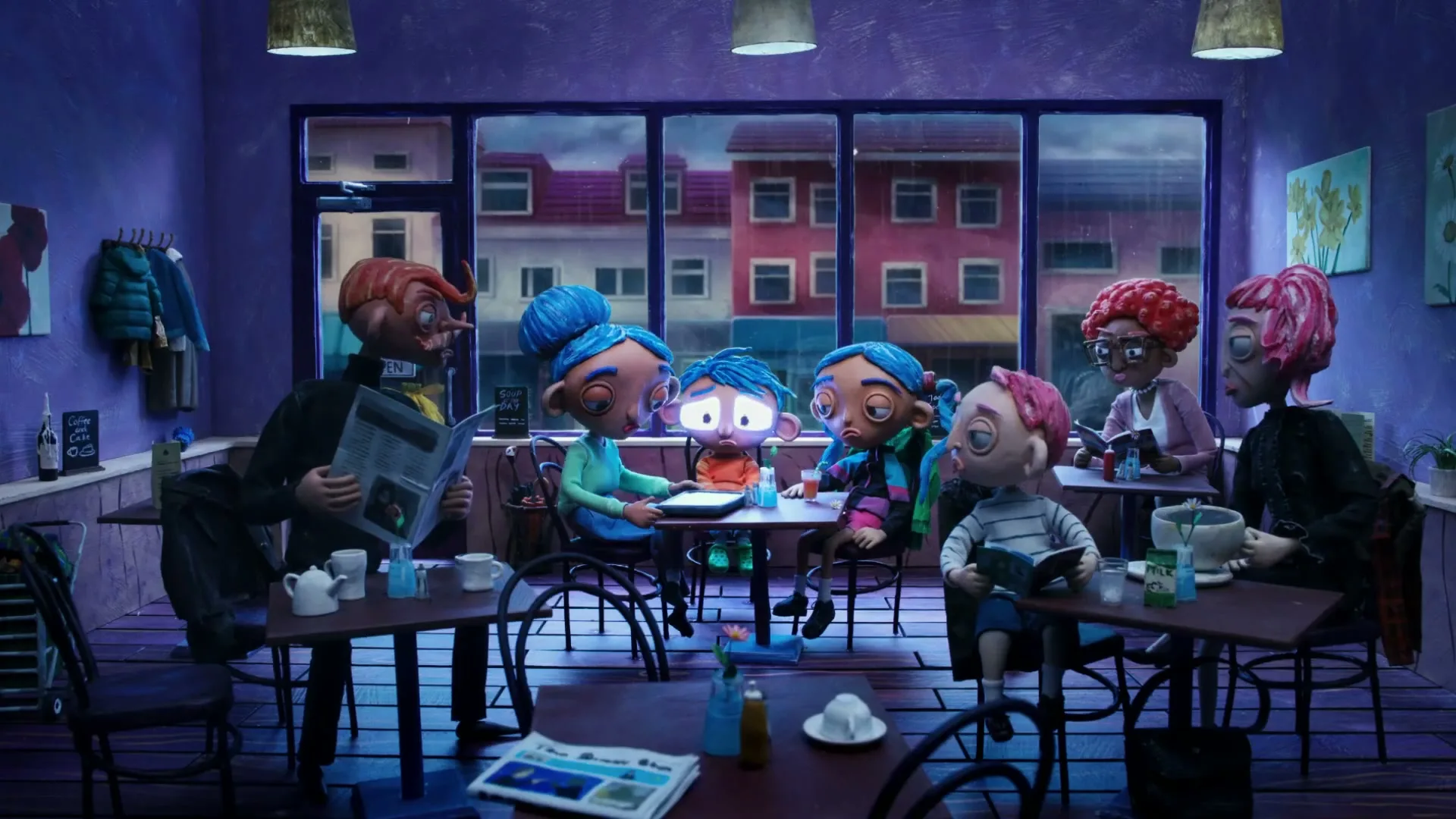 A group of stop-motion animated characters are sitting at tables in a cafe, with one character's face distorting as they watch a glowing screen.