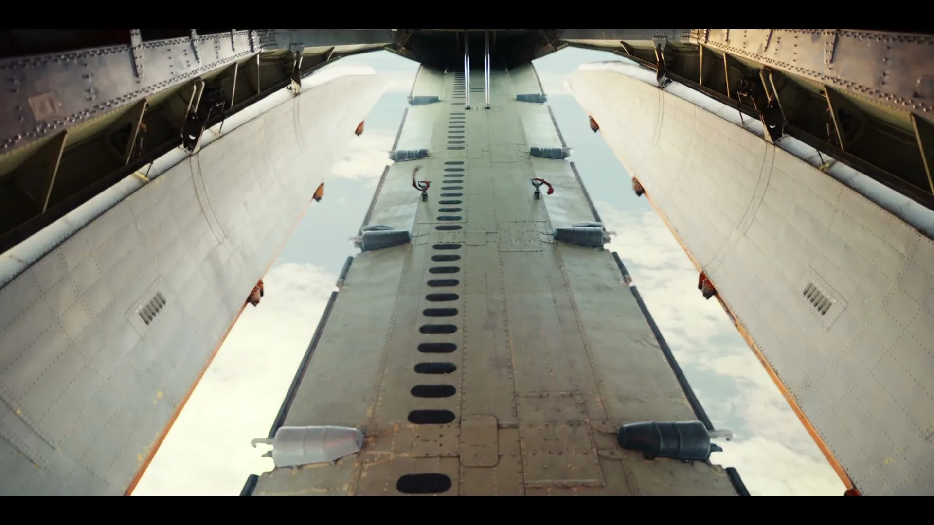 A wide shot from inside a cargo plane looking out the back ramp at the sky, with the ramp slowly lowering.