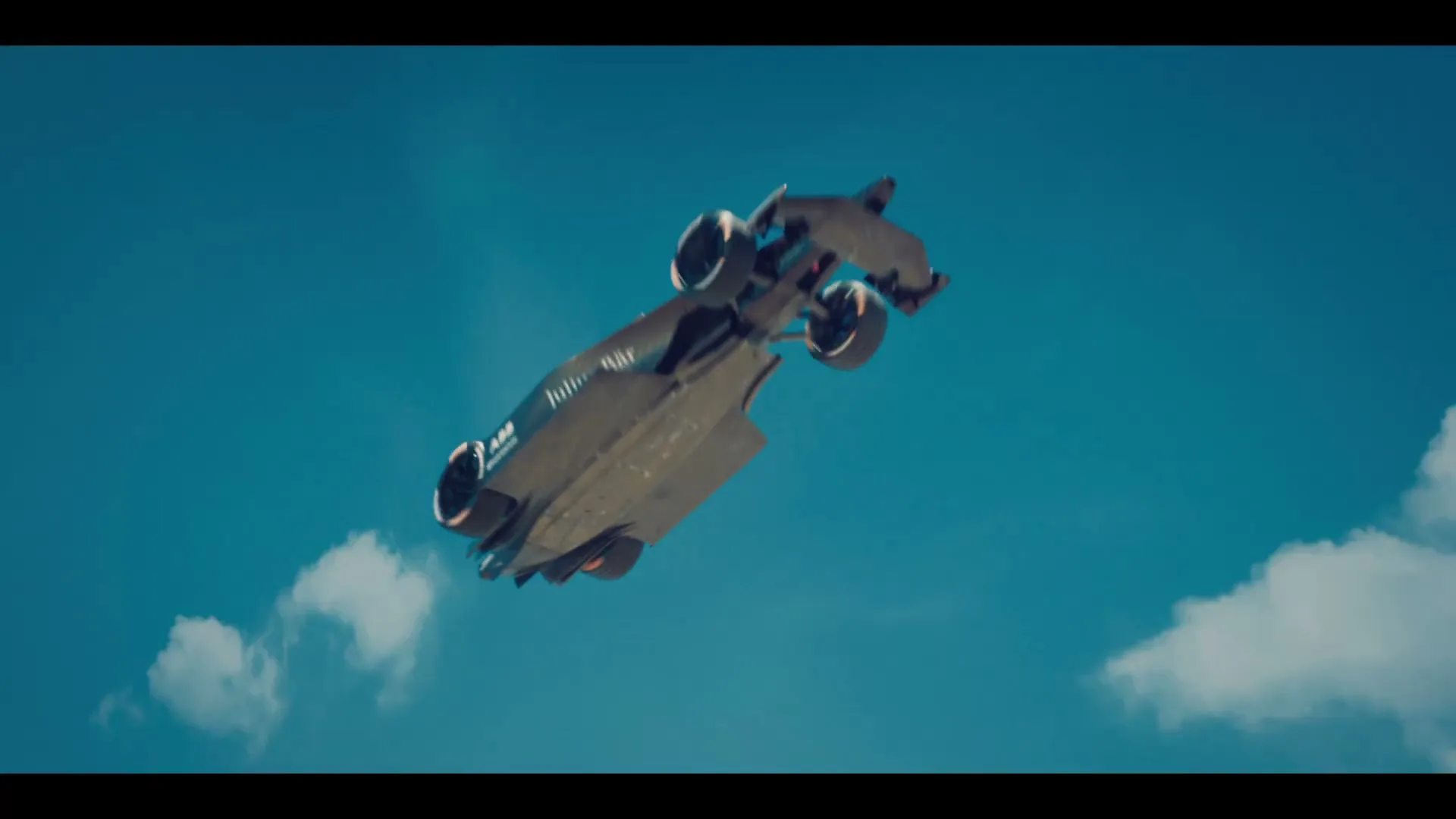 A Formula E race car, sleek and futuristic, flies through a bright blue sky with scattered white clouds.