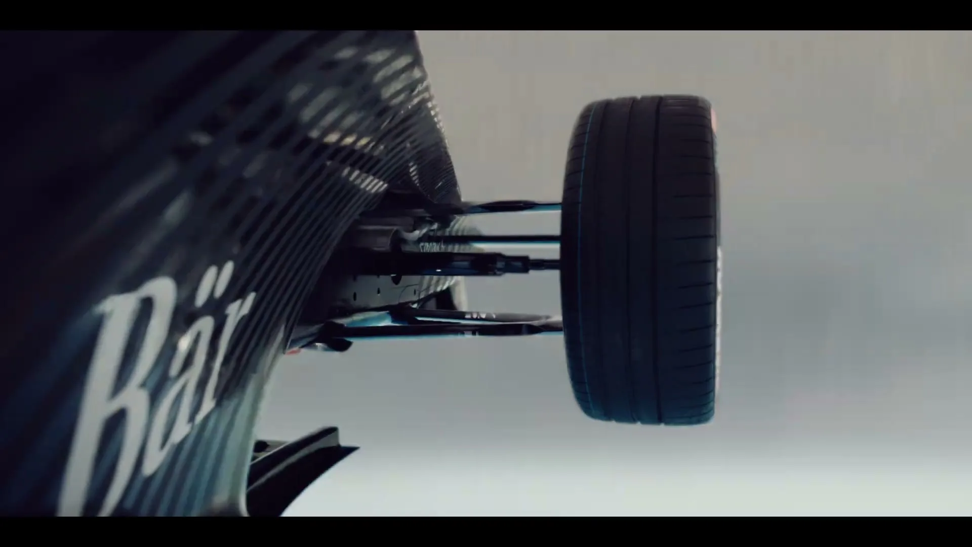 A close-up shot of a Formula E race car's front wheel and suspension, with the car moving at high speed against a blurred background.