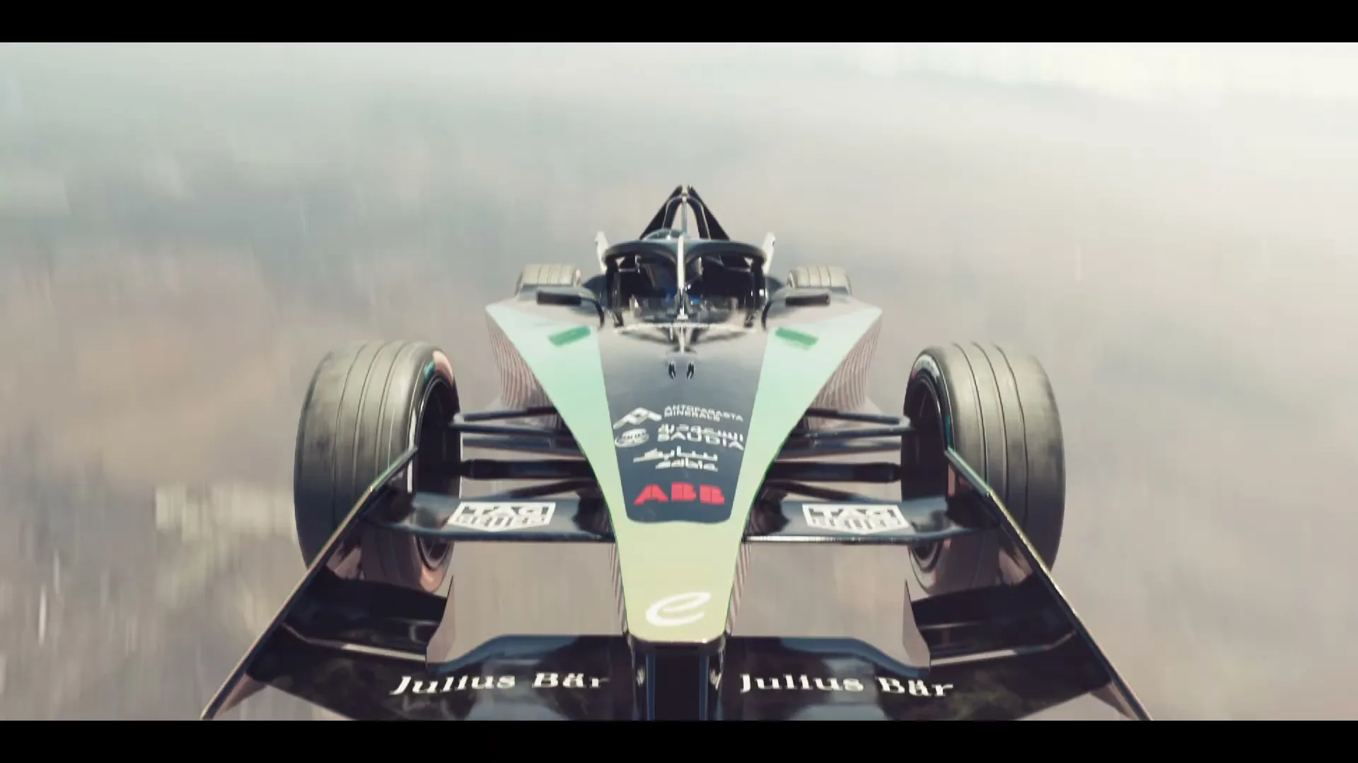 A Formula E race car, black and green, speeds forward on a track, with the camera positioned directly in front of it.