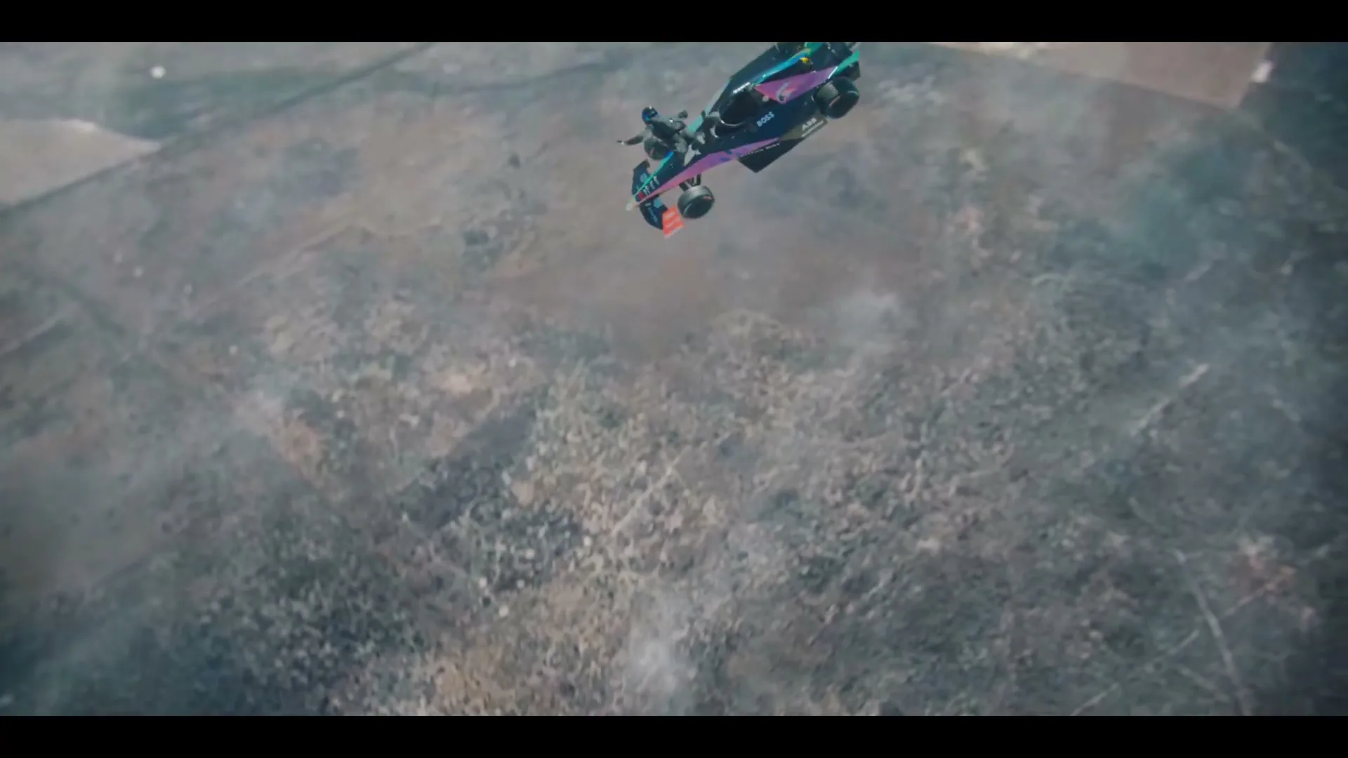 A Formula E race car and a skydiver freefall together through the sky, with vast, barren land visible far below.